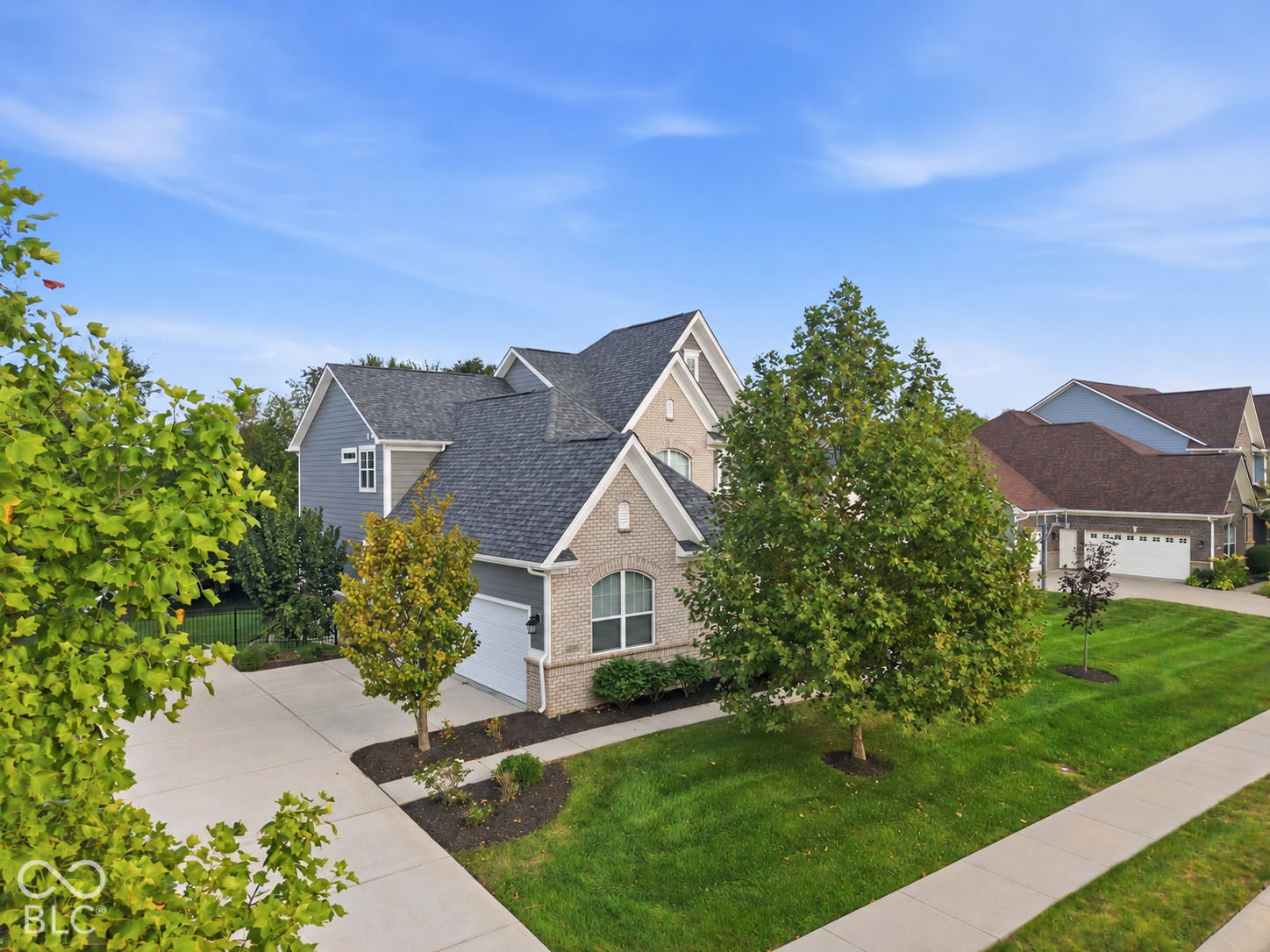 Two-story gray and brick home with a multi-gabled roof, attached garage, and landscaped front lawn.