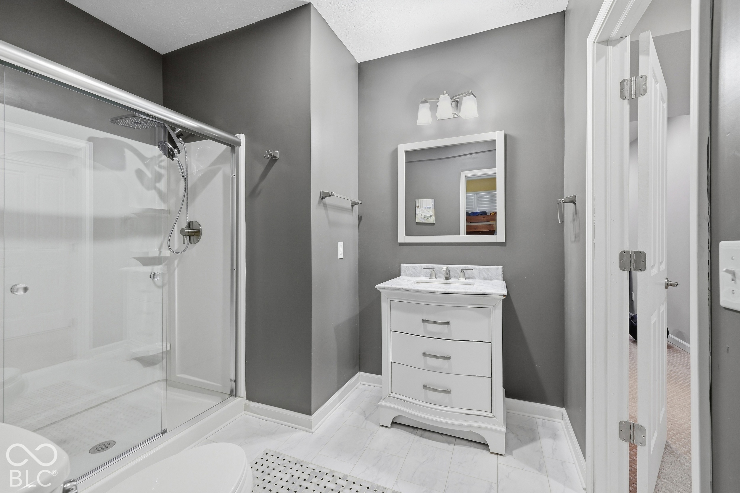 Bathroom with a glass walk-in shower, white vanity, framed mirror, and bathtub edge in the foreground.