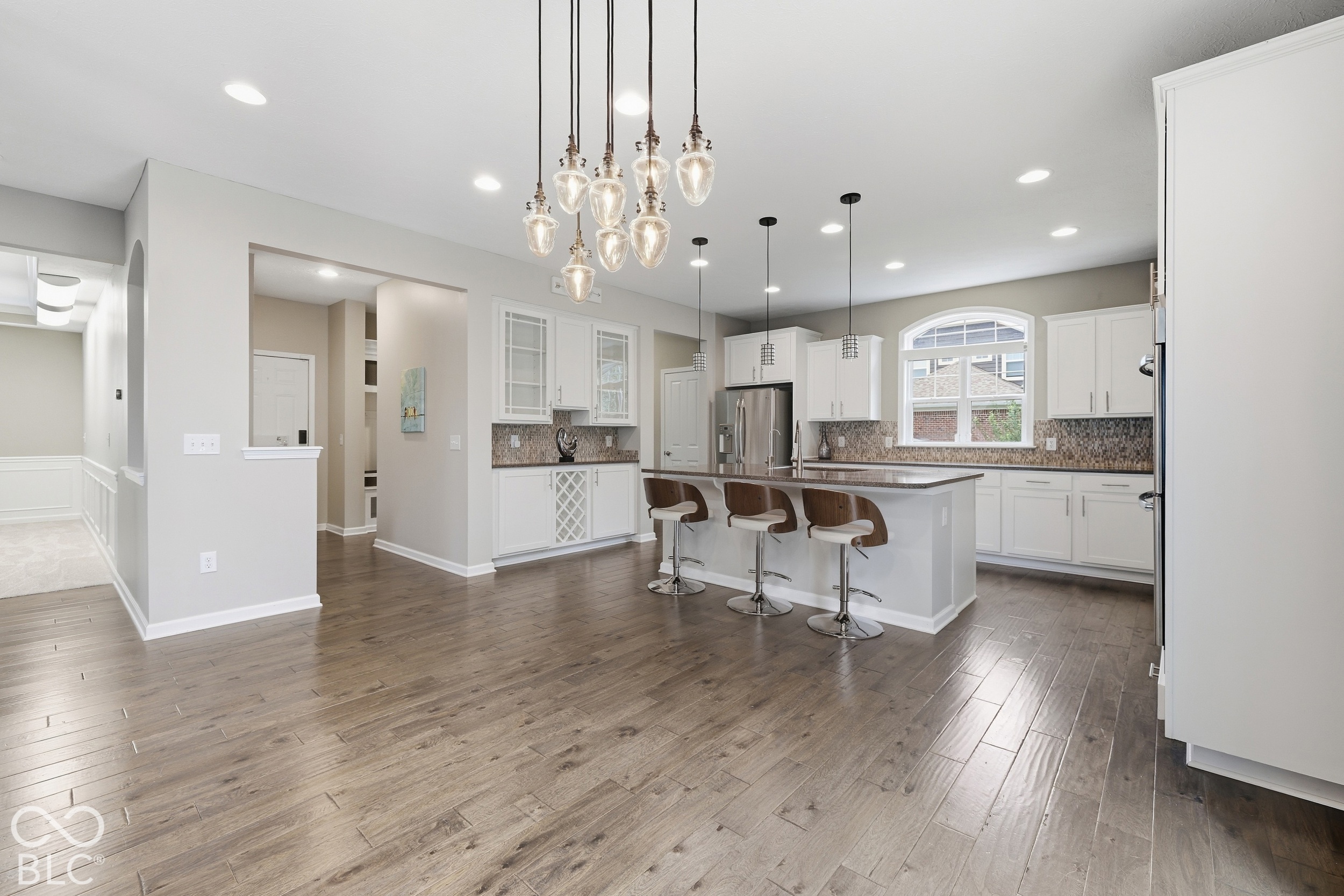 Open kitchen with white cabinets, a large island, three stools, and wood-look flooring.