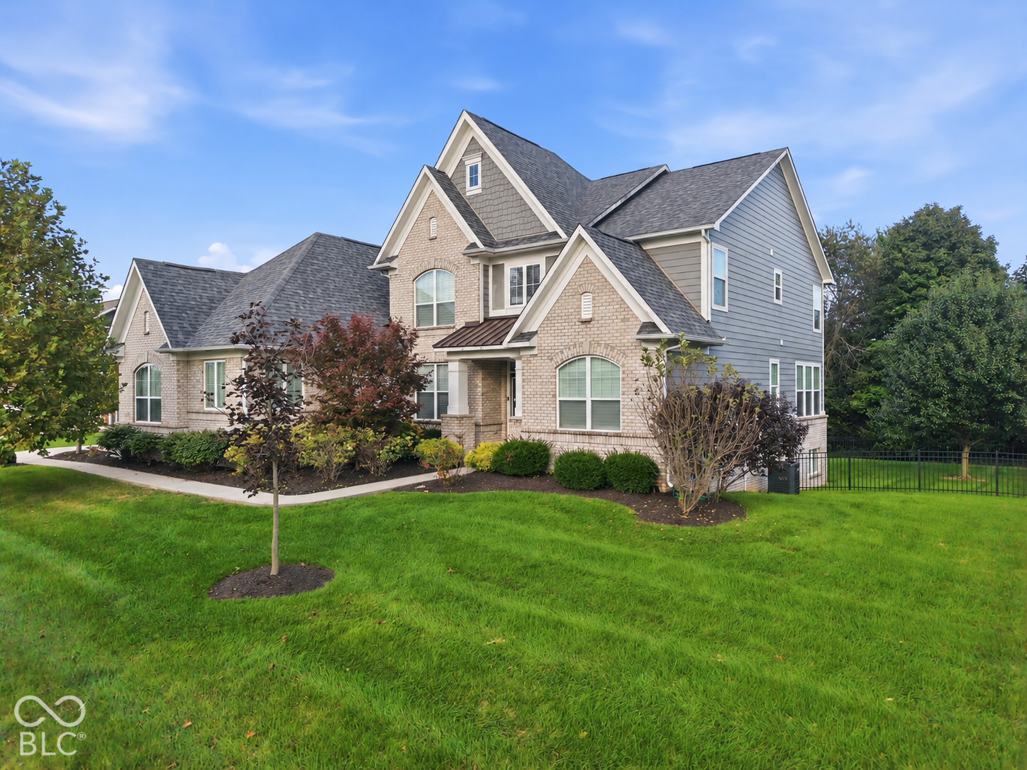 Two-story brick and gray-sided home with multiple gables and a landscaped front lawn.