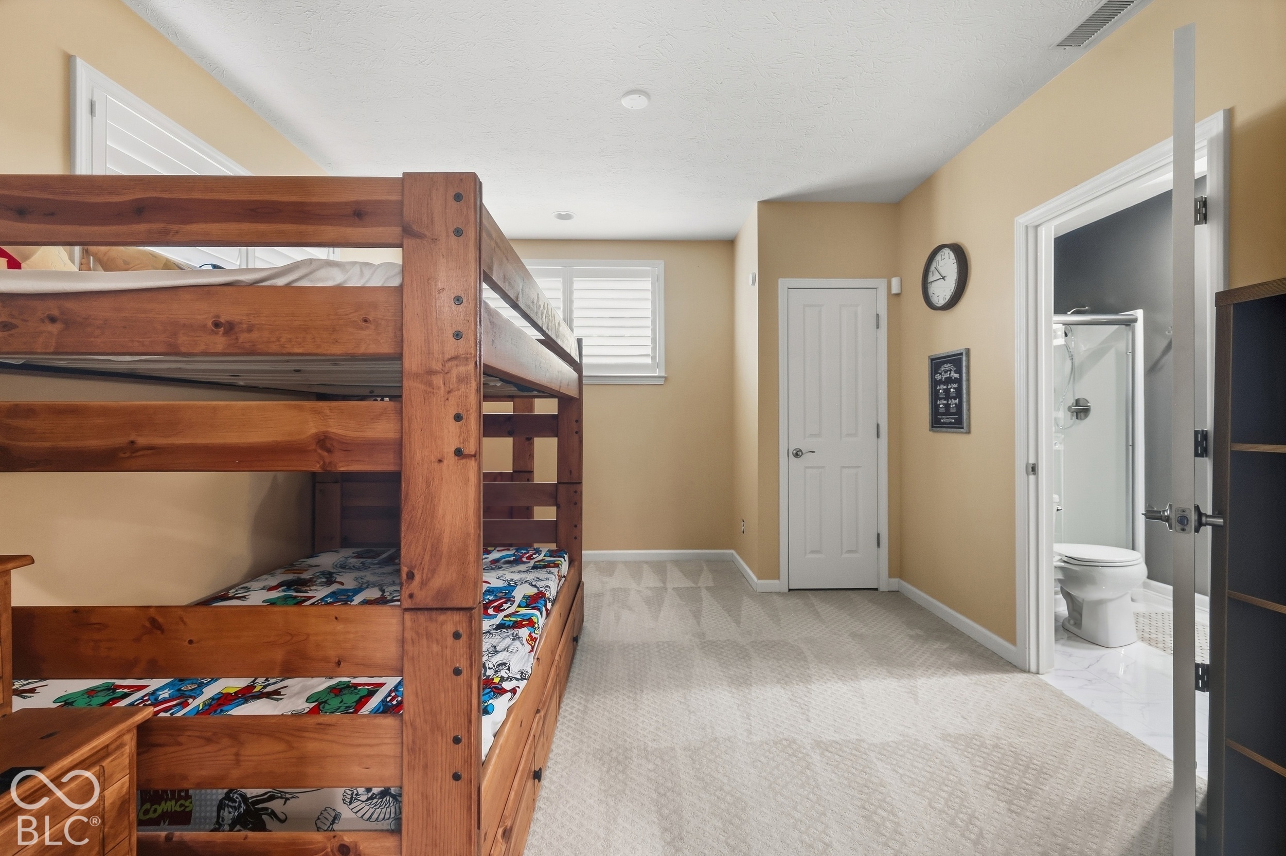 Bedroom with a wooden bunk bed and colorful comic-book bedding beside an open bathroom doorway.