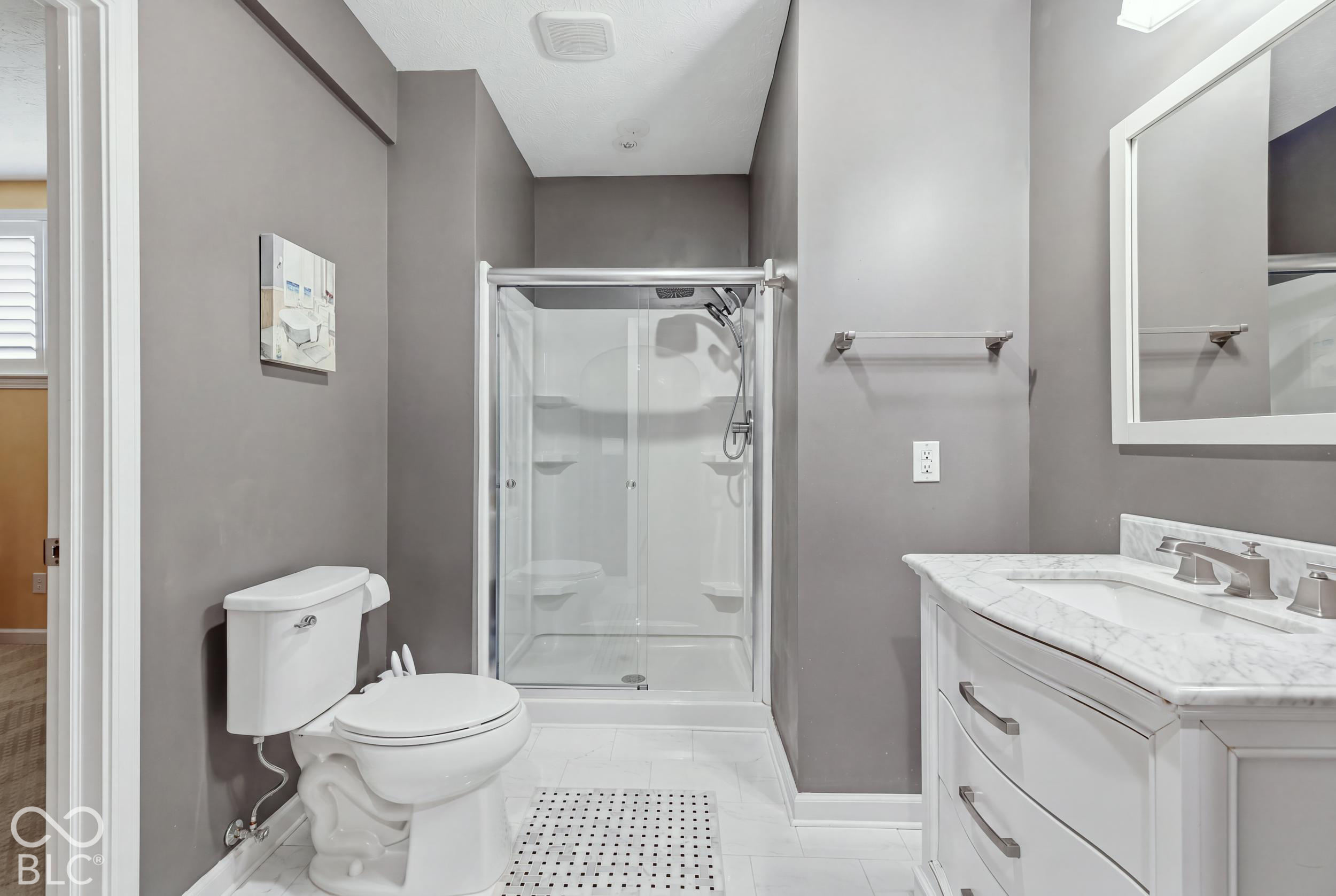 Bathroom with a glass-enclosed shower, white toilet, and marble-look vanity.