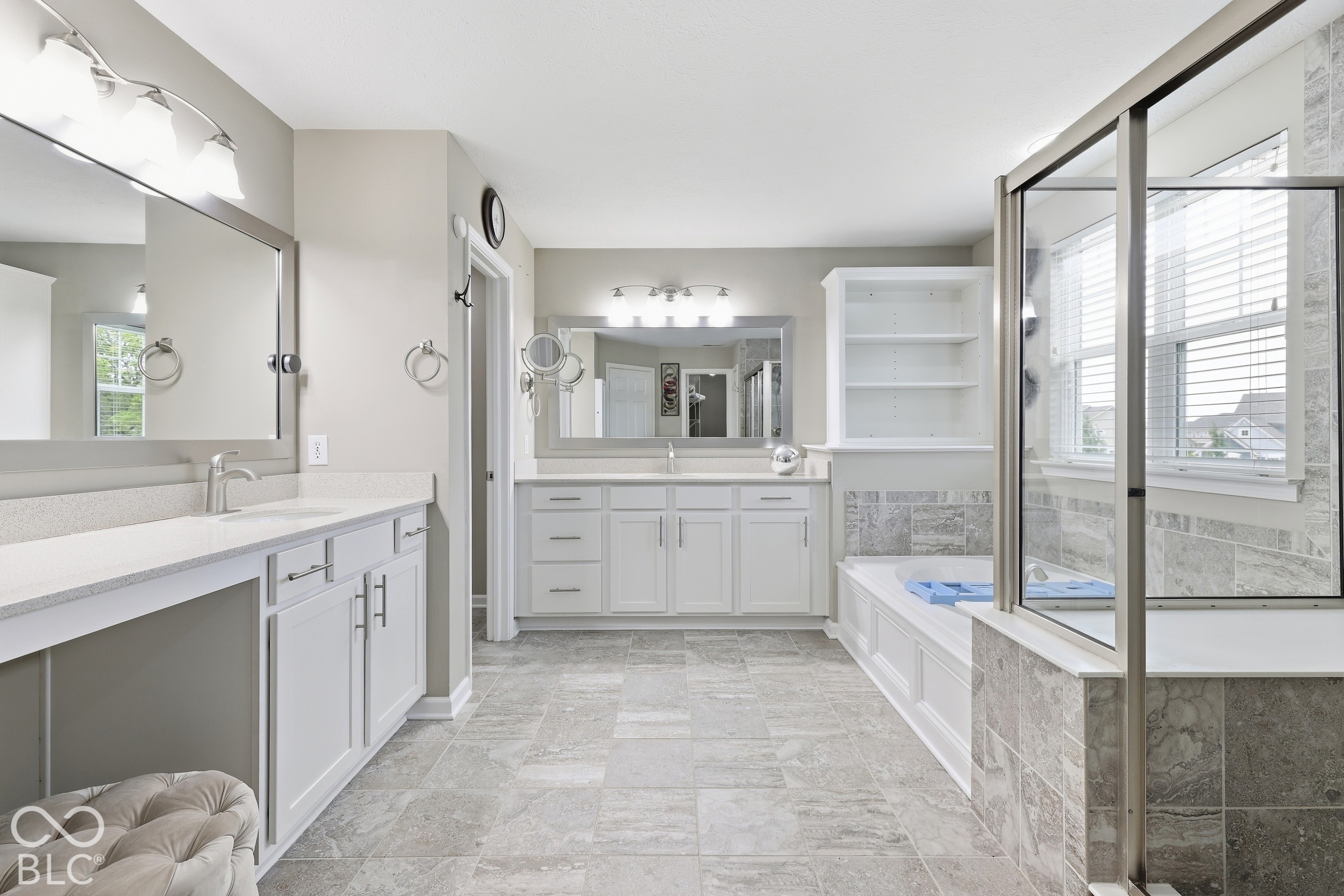 Bathroom with a white double vanity, gray tile, soaking tub, and glass-enclosed shower.