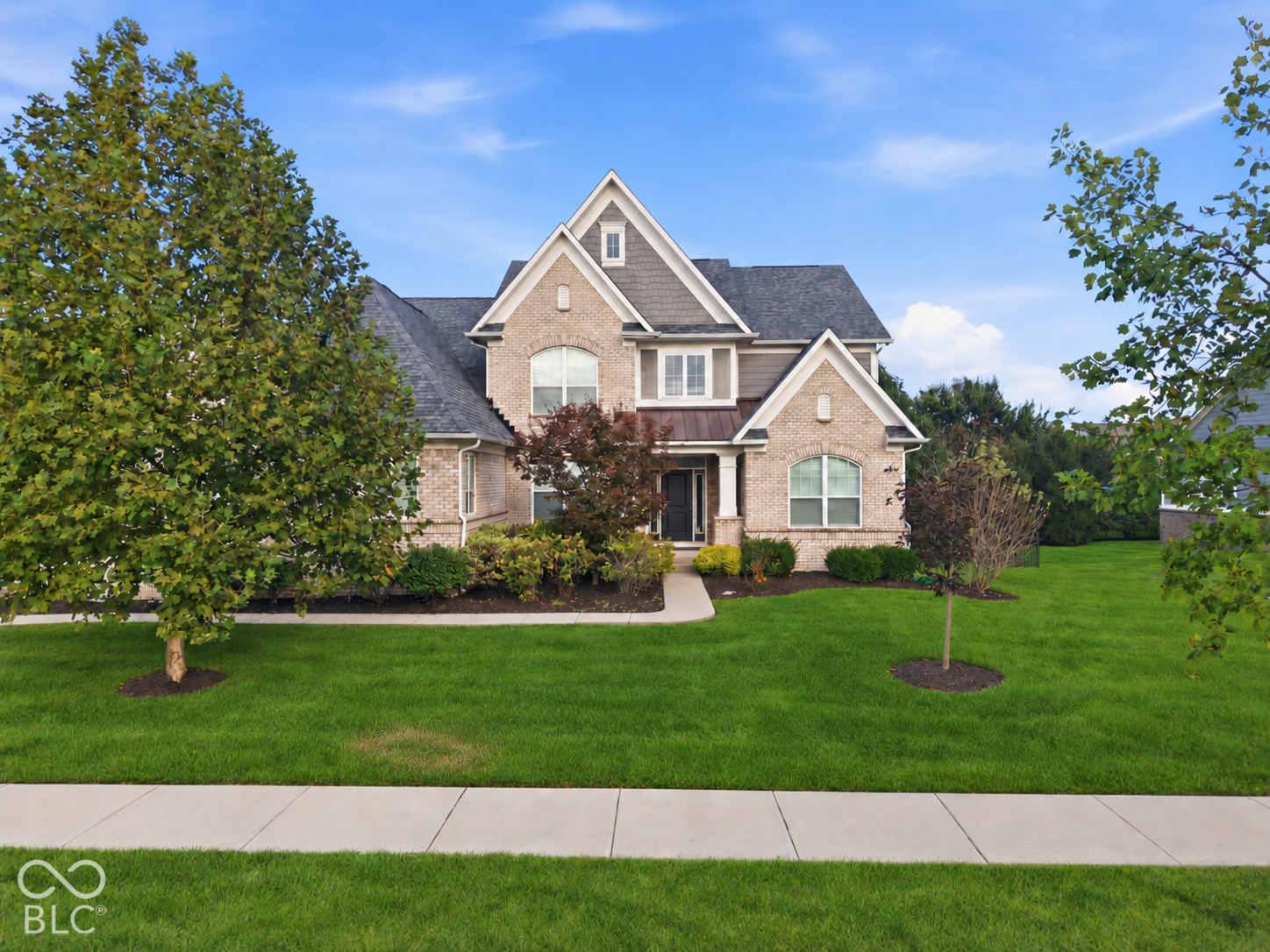 Two-story brick house with steep gables, landscaped gardens, and a broad green front lawn.