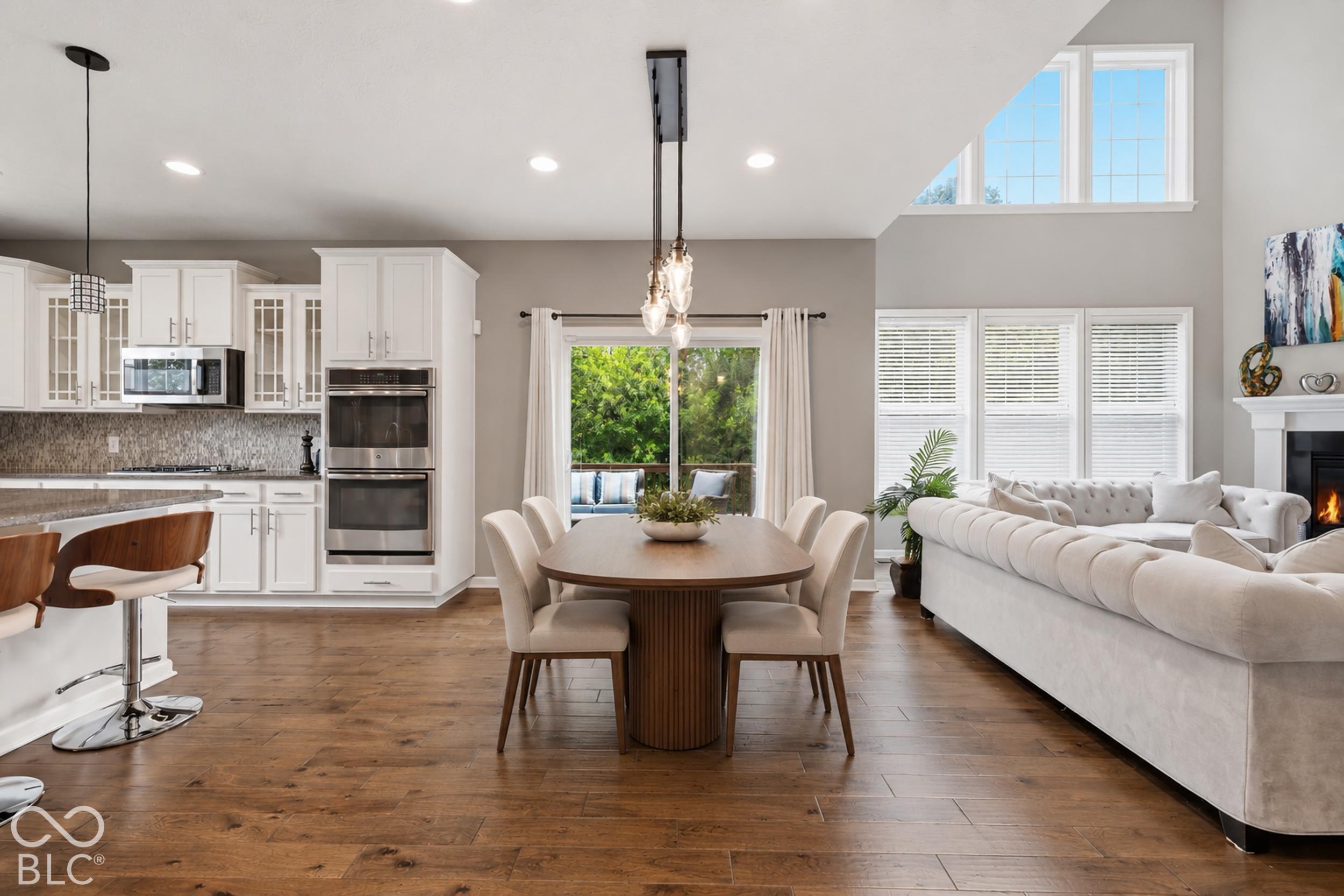 Open-plan kitchen, dining, and living room with white cabinetry, a wood table, and a white sectional.