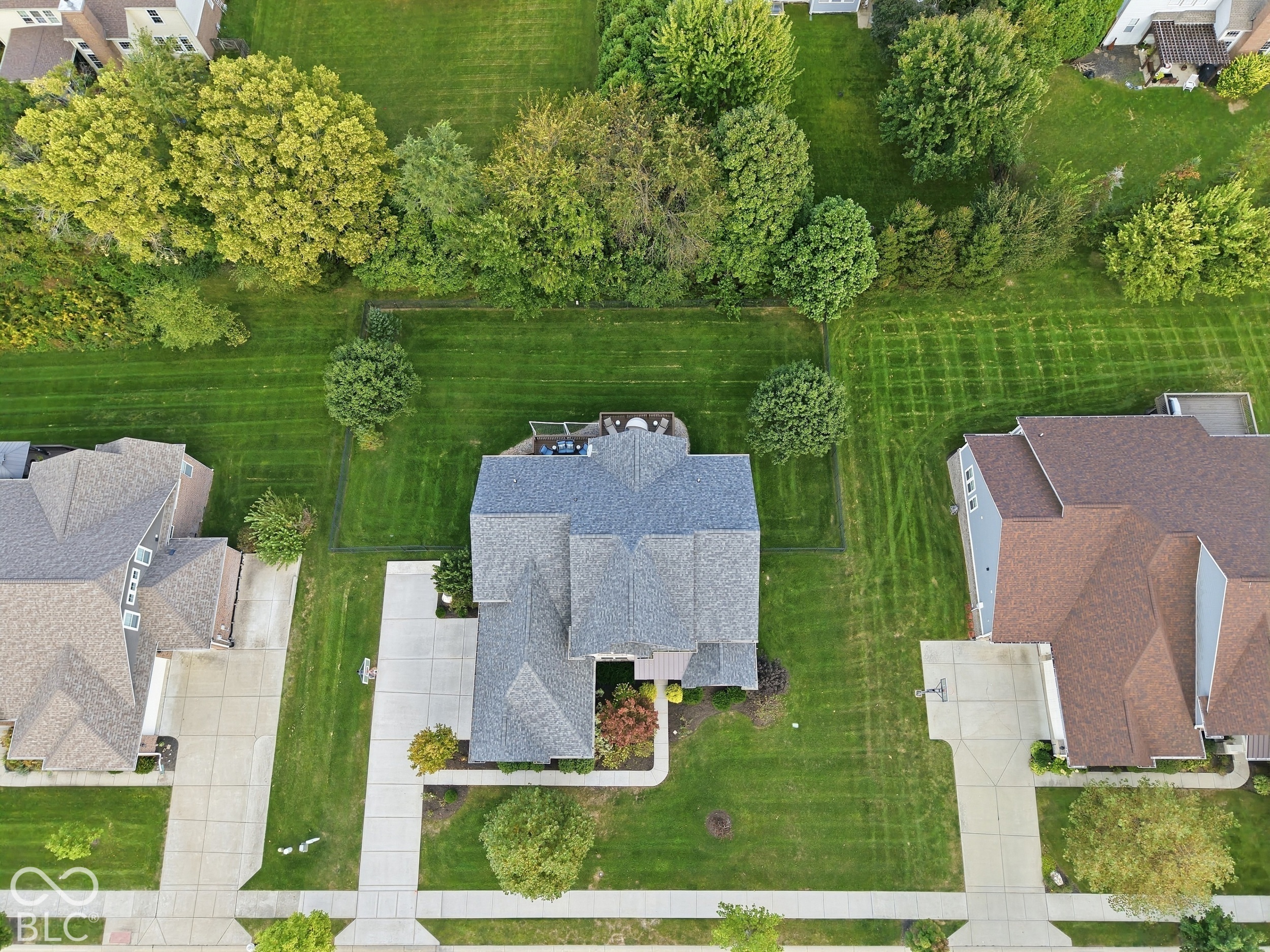 Aerial view of a home with a fenced, tree-lined backyard and rear deck.