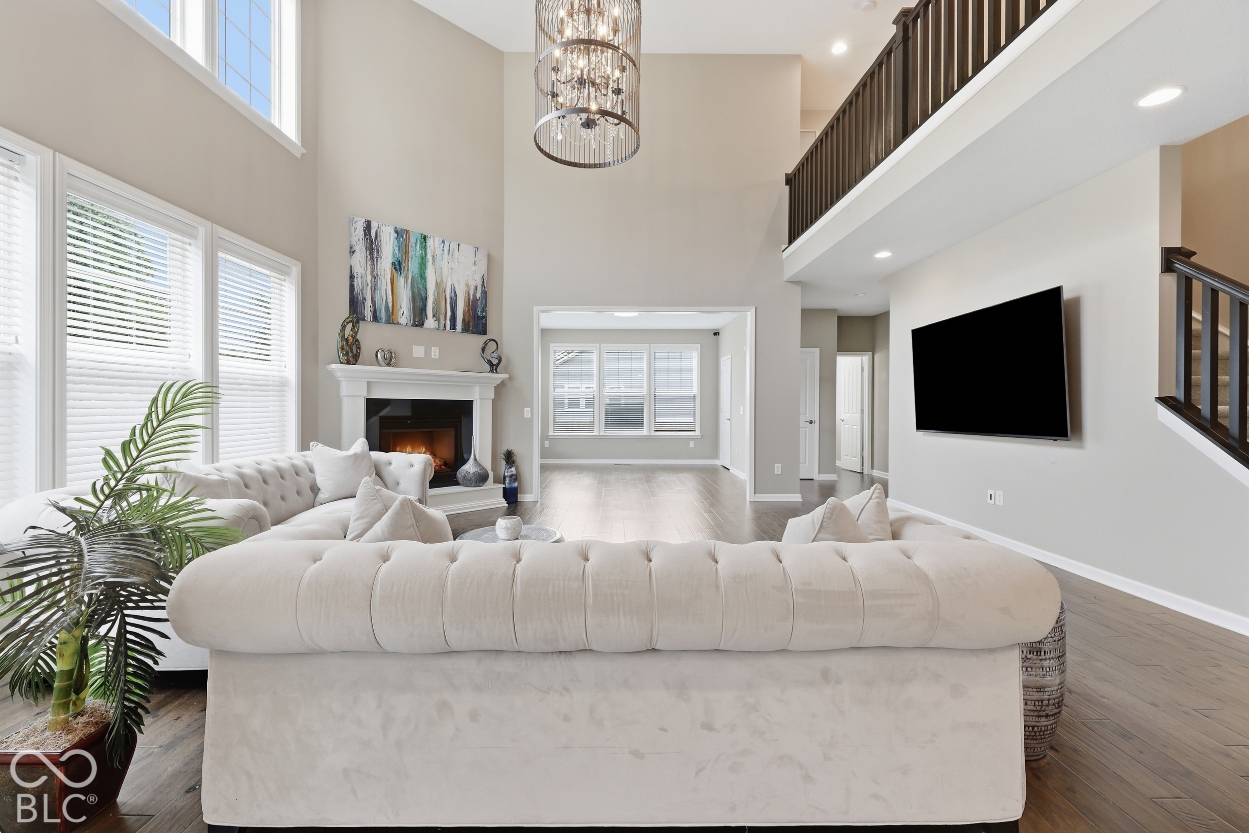 Two-story living room with a white sectional, fireplace, chandelier, and upper-level railing.