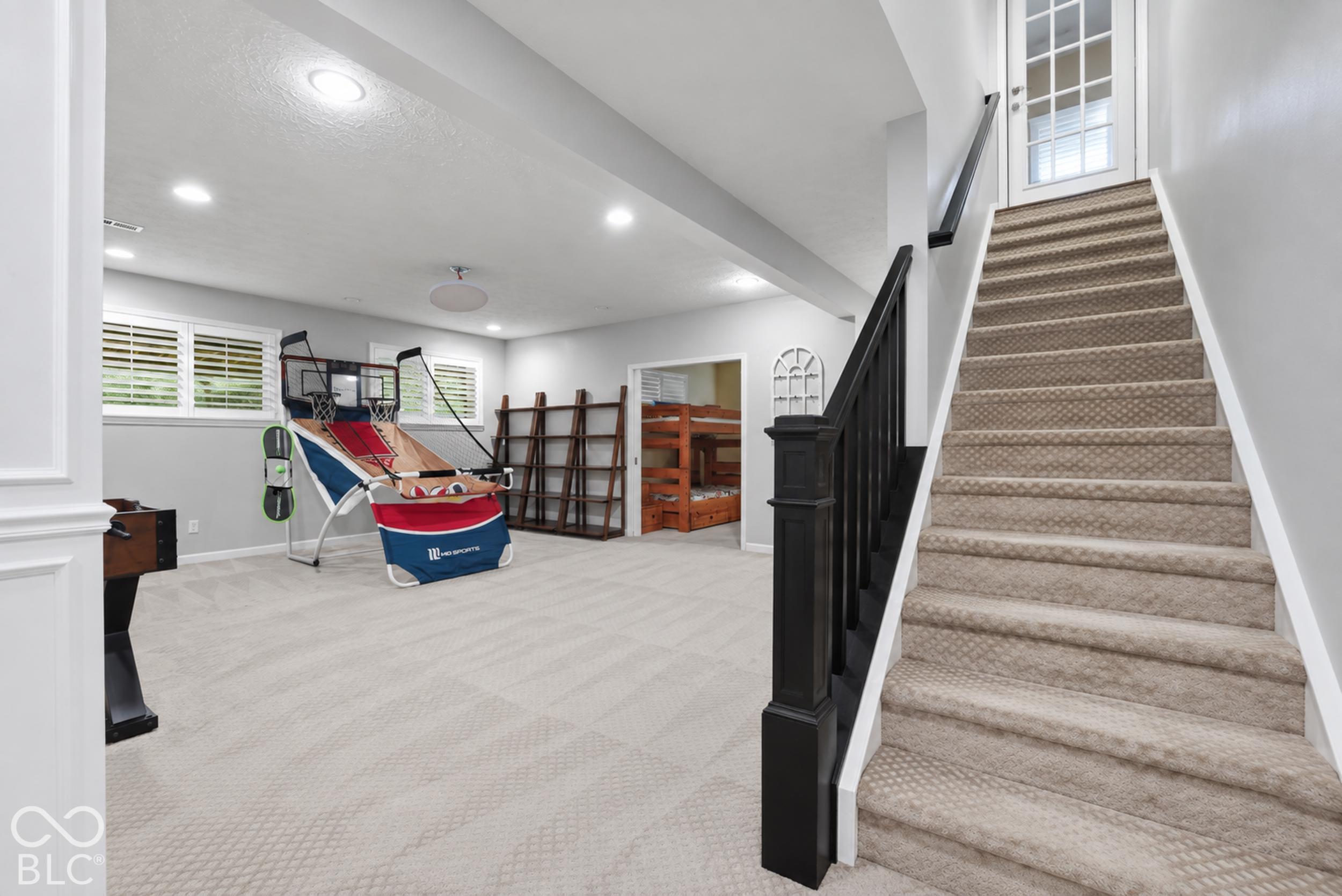 Lower-level recreation room with a carpeted staircase, basketball arcade game, and wooden bunk beds.