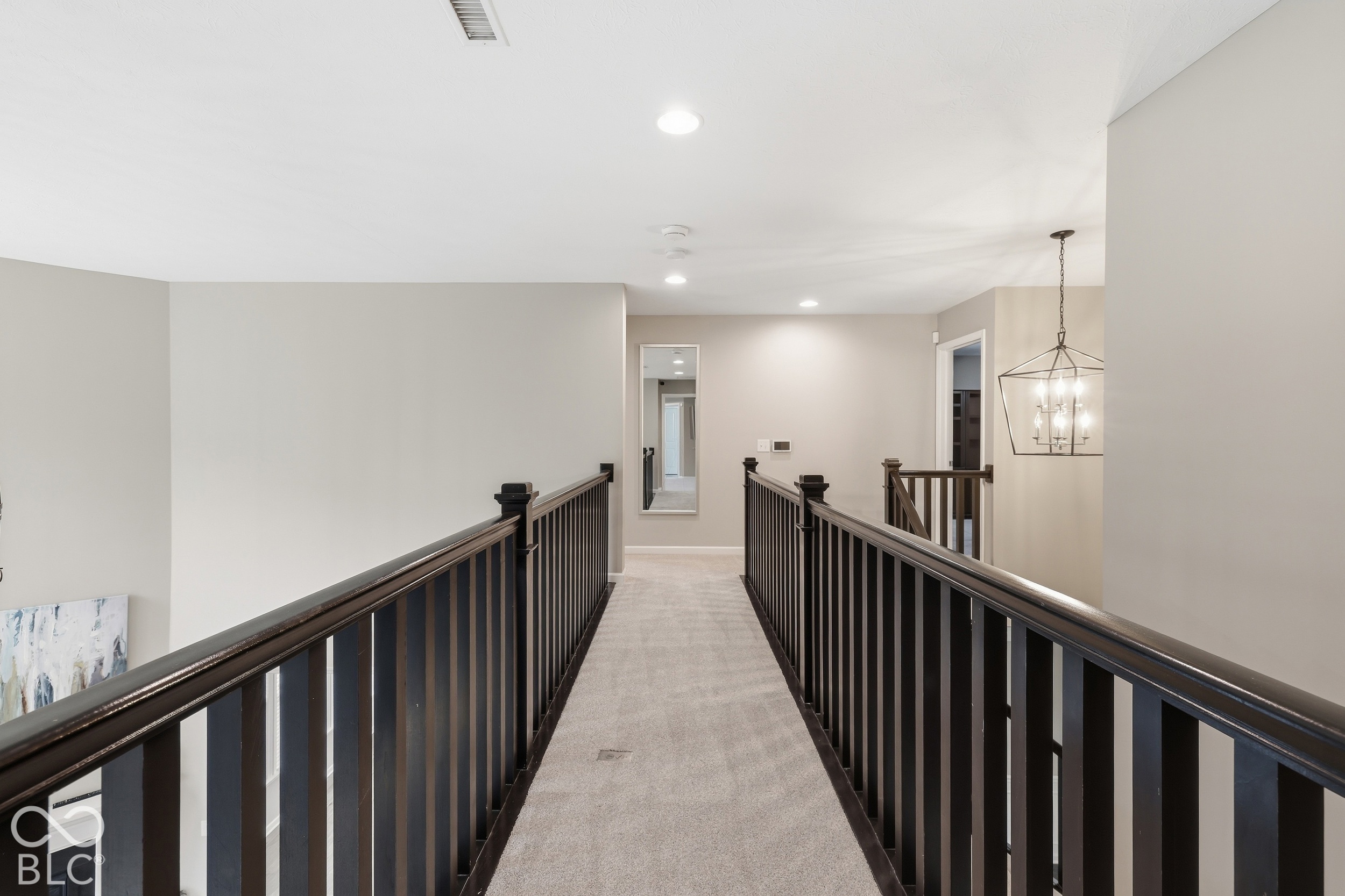 Carpeted upstairs landing with dark wood railings and a hanging chandelier.
