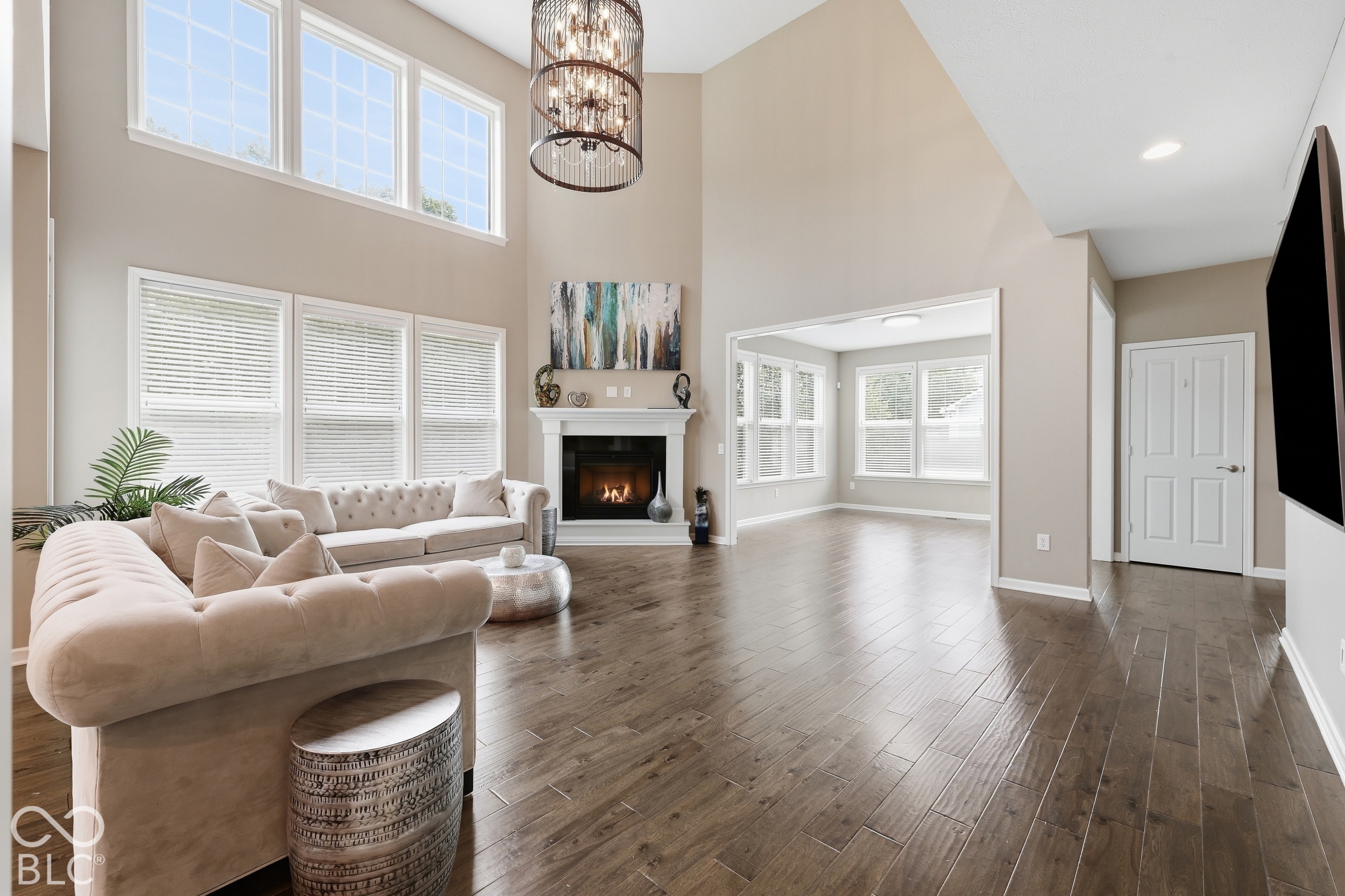 Staged living room with vaulted ceiling, tall windows, fireplace, and chandelier.