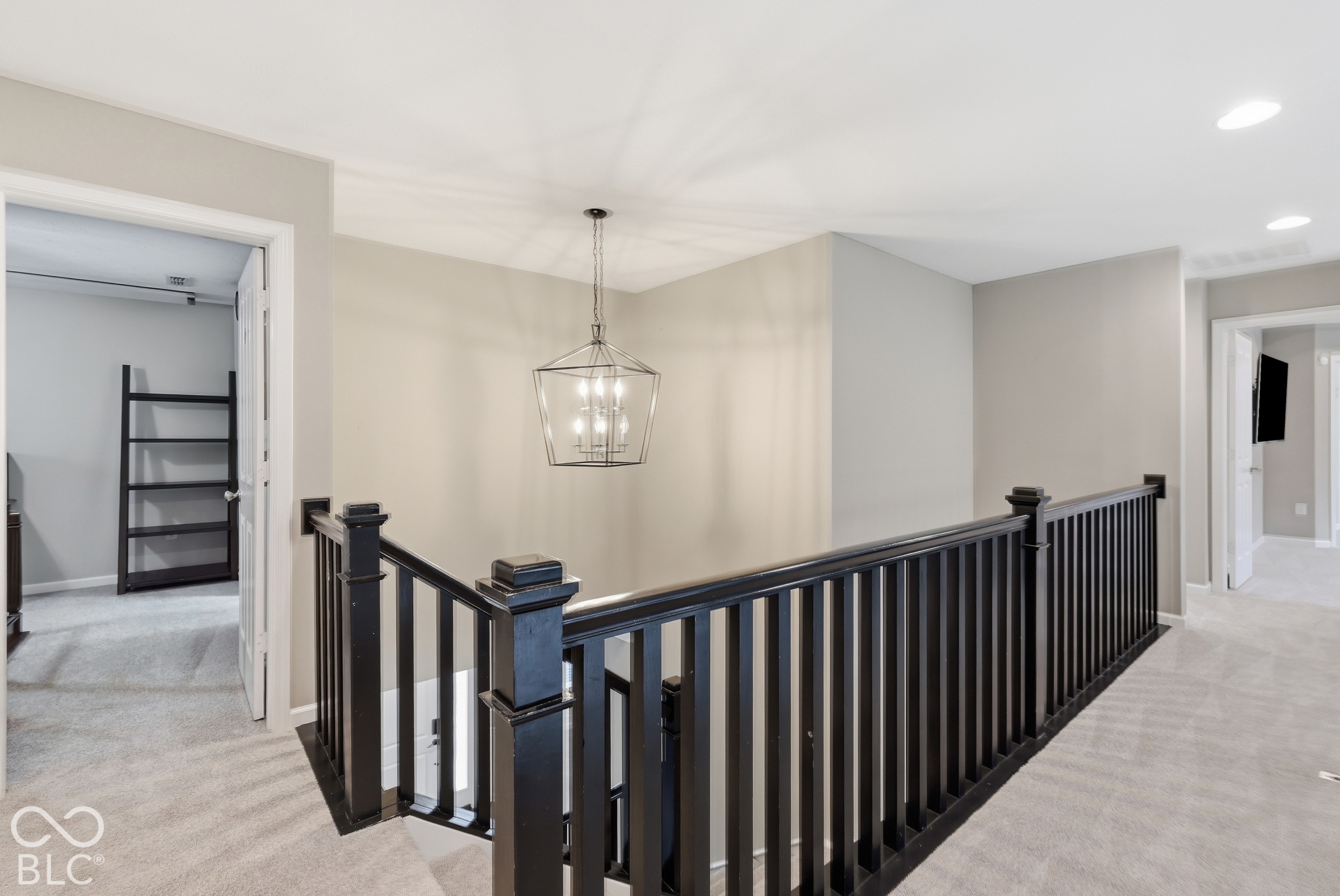 Carpeted upstairs landing with a dark wood stair railing and geometric hanging chandelier.