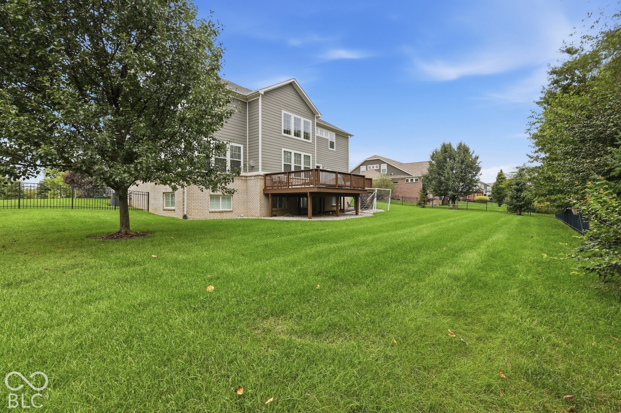 Home’s rear exterior with a raised deck, fenced lawn, and mature trees.