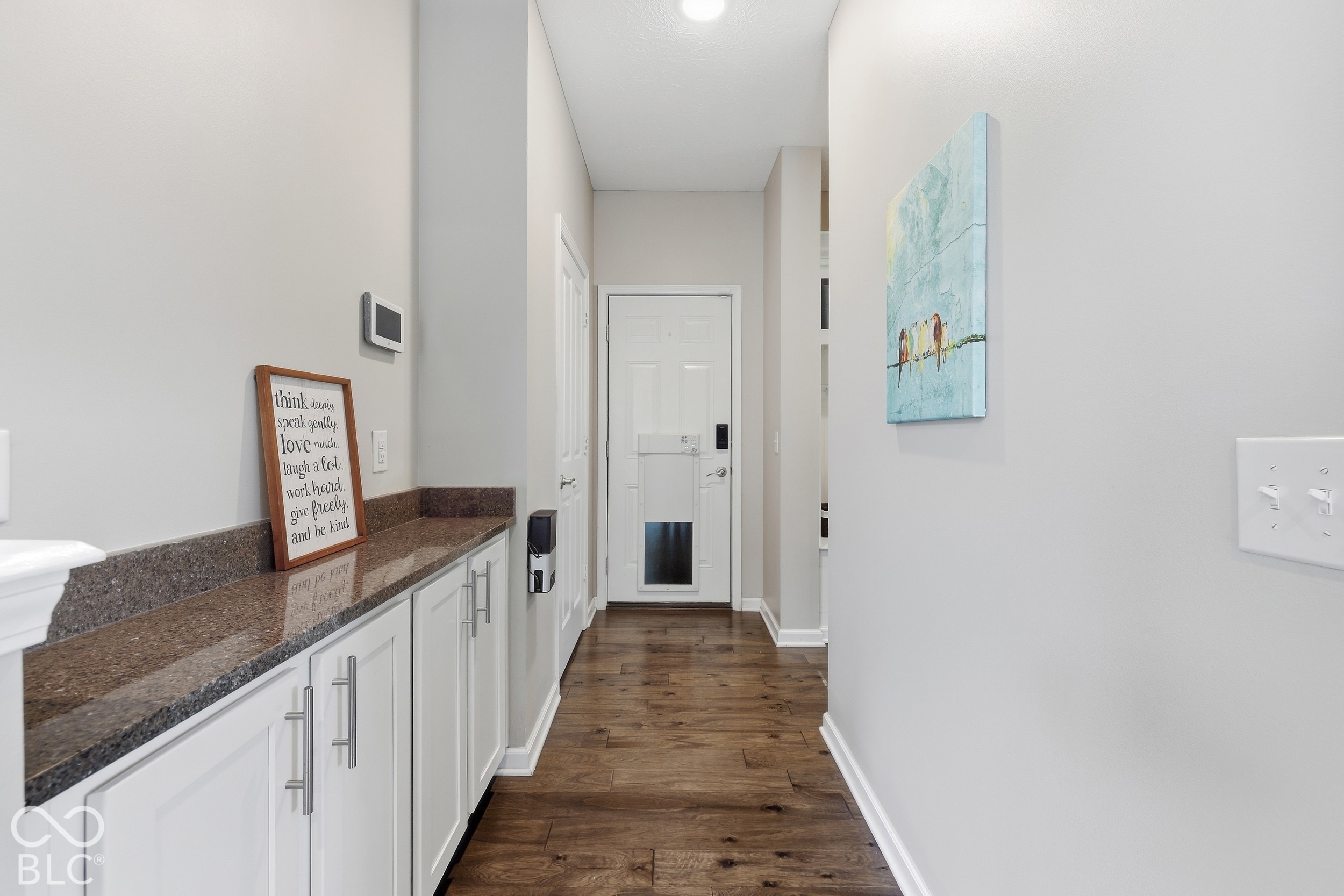 Entry hallway with white storage cabinets, a dark stone countertop, warm wood flooring, and the front door.