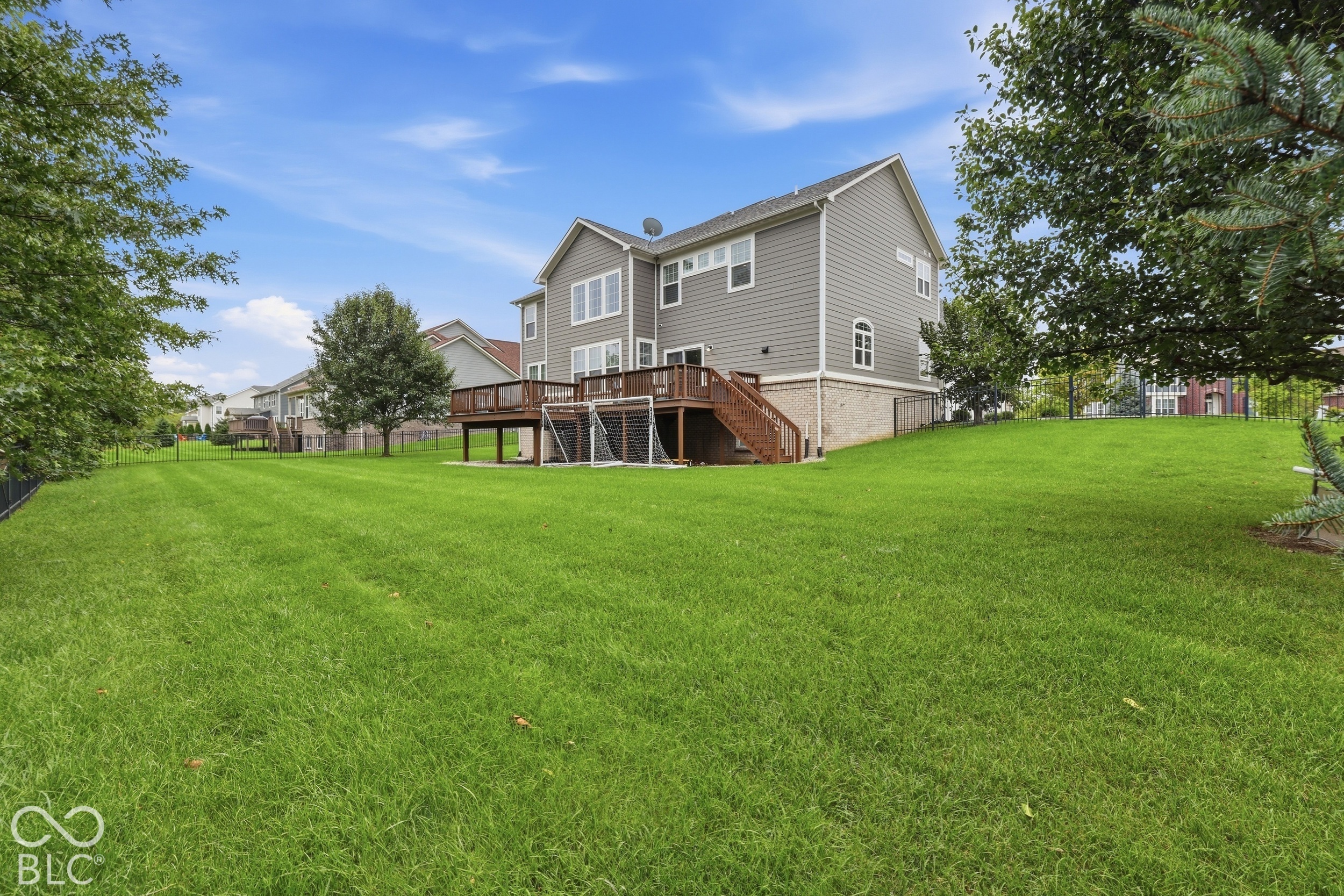 Rear of a two-story gray house with a raised deck, soccer goal, and broad fenced lawn.