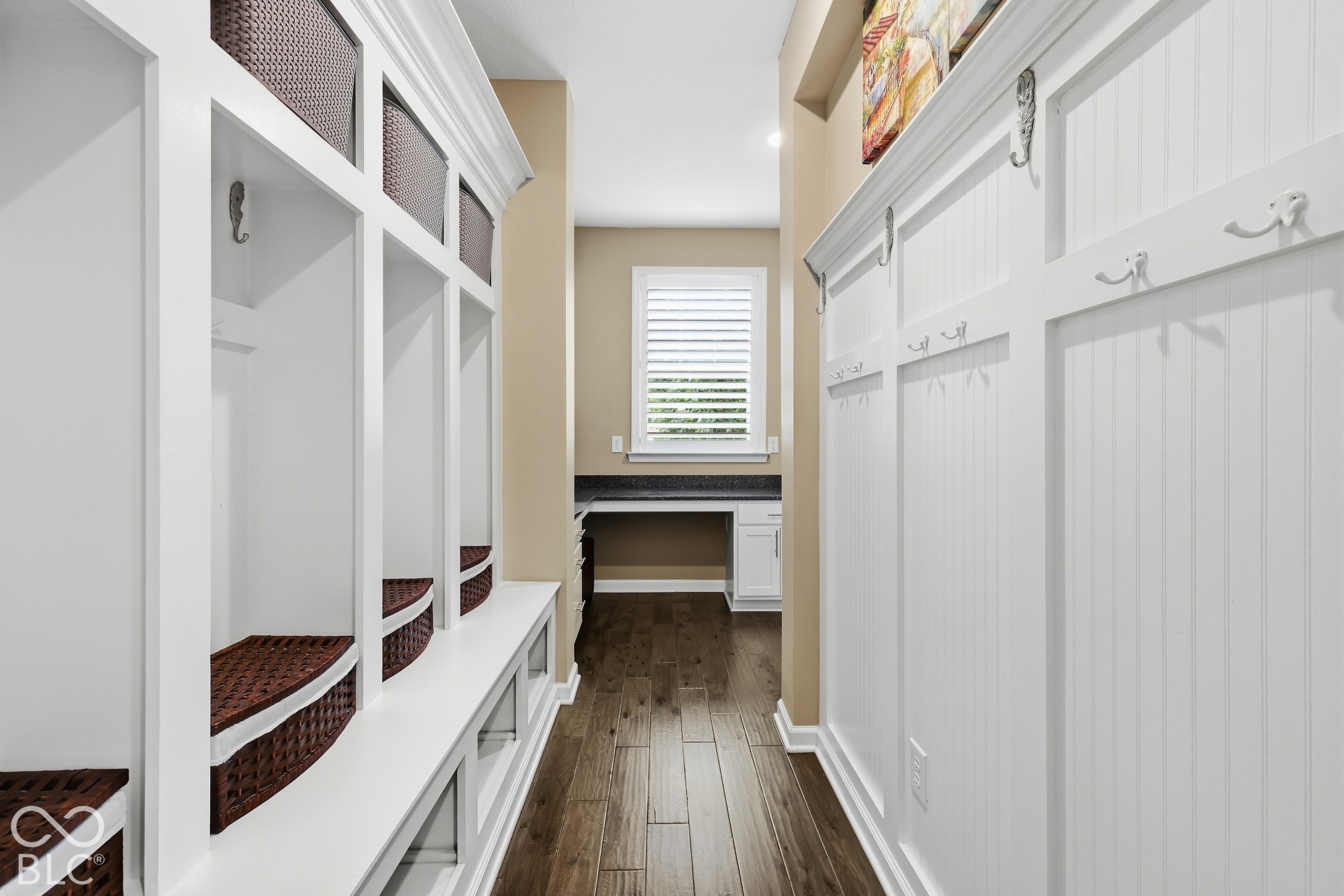 Mudroom with white cubbies and woven baskets beside a paneled wall with hooks.