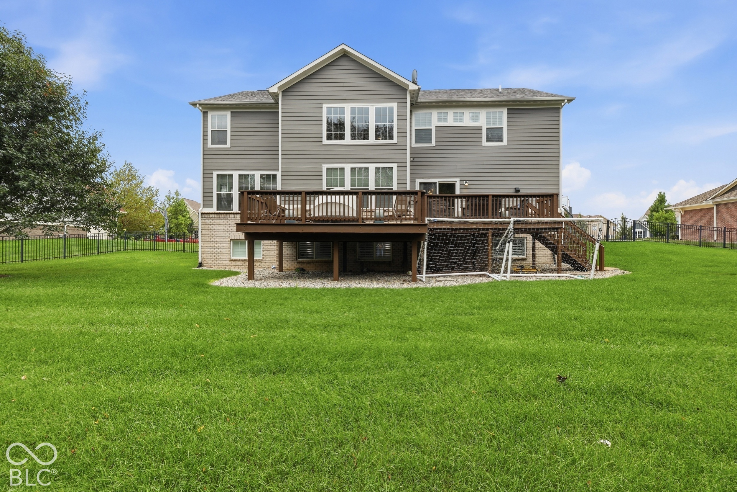 Rear of a two-story gray house with a raised wooden deck and a large lawn.