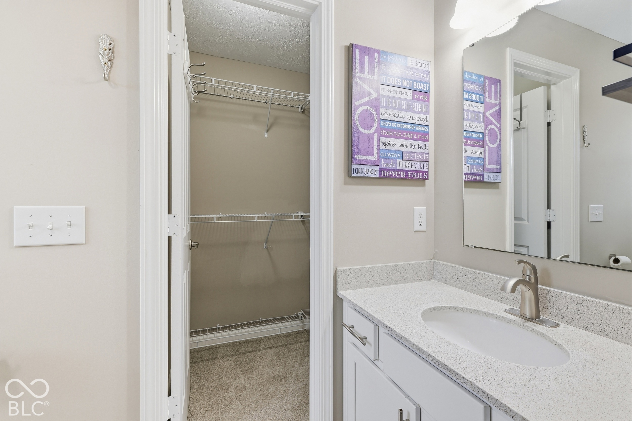 Bathroom vanity and mirror beside an open walk-in closet with wire shelving.