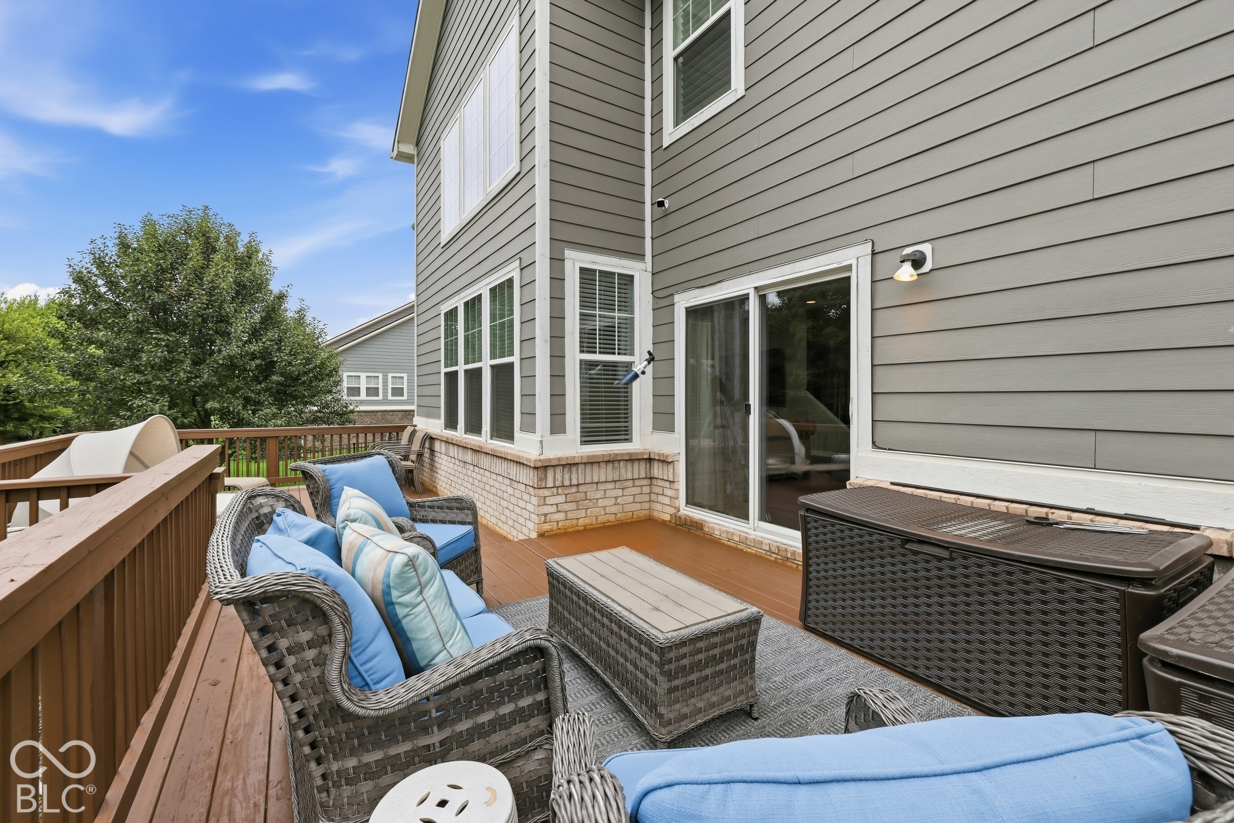 Furnished deck with blue-cushioned wicker seating beside the home’s sliding glass doors.