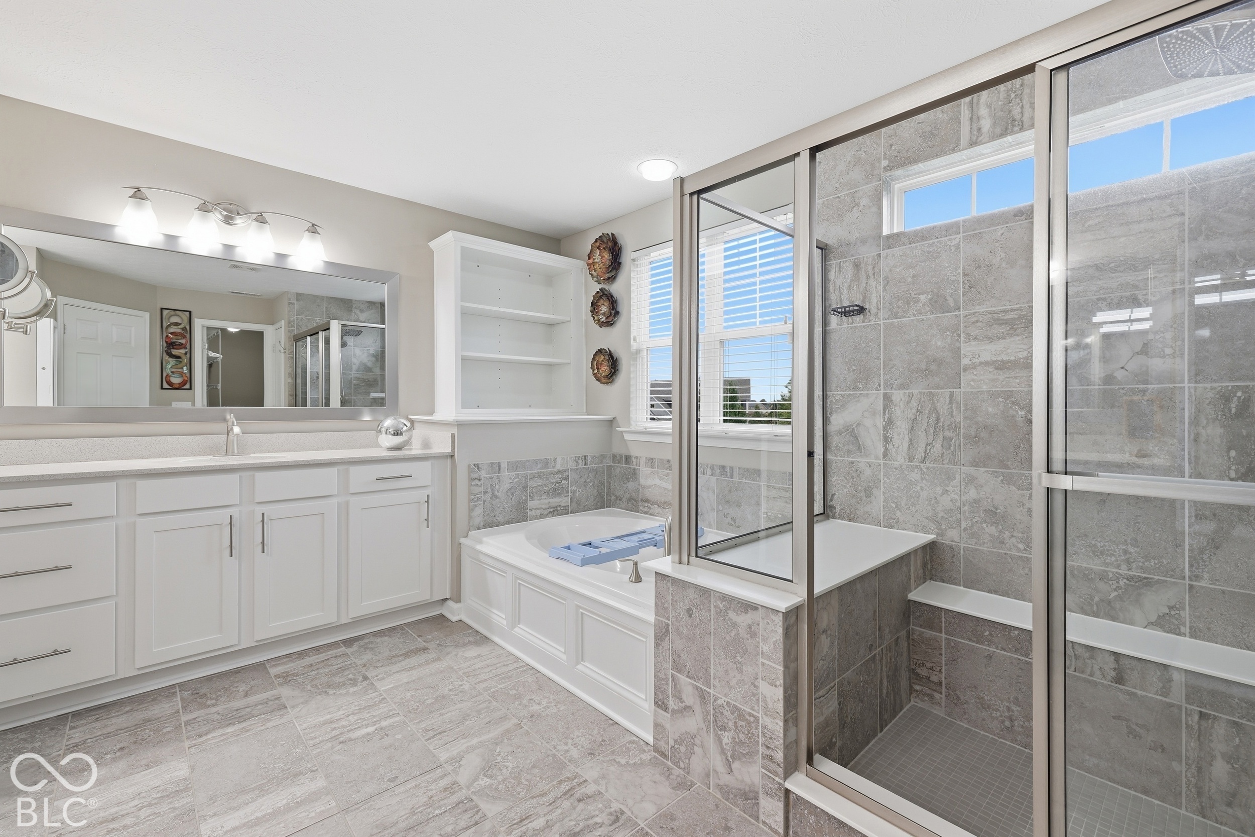 Bathroom with white vanity, built-in tub, and separate glass shower with gray tile.