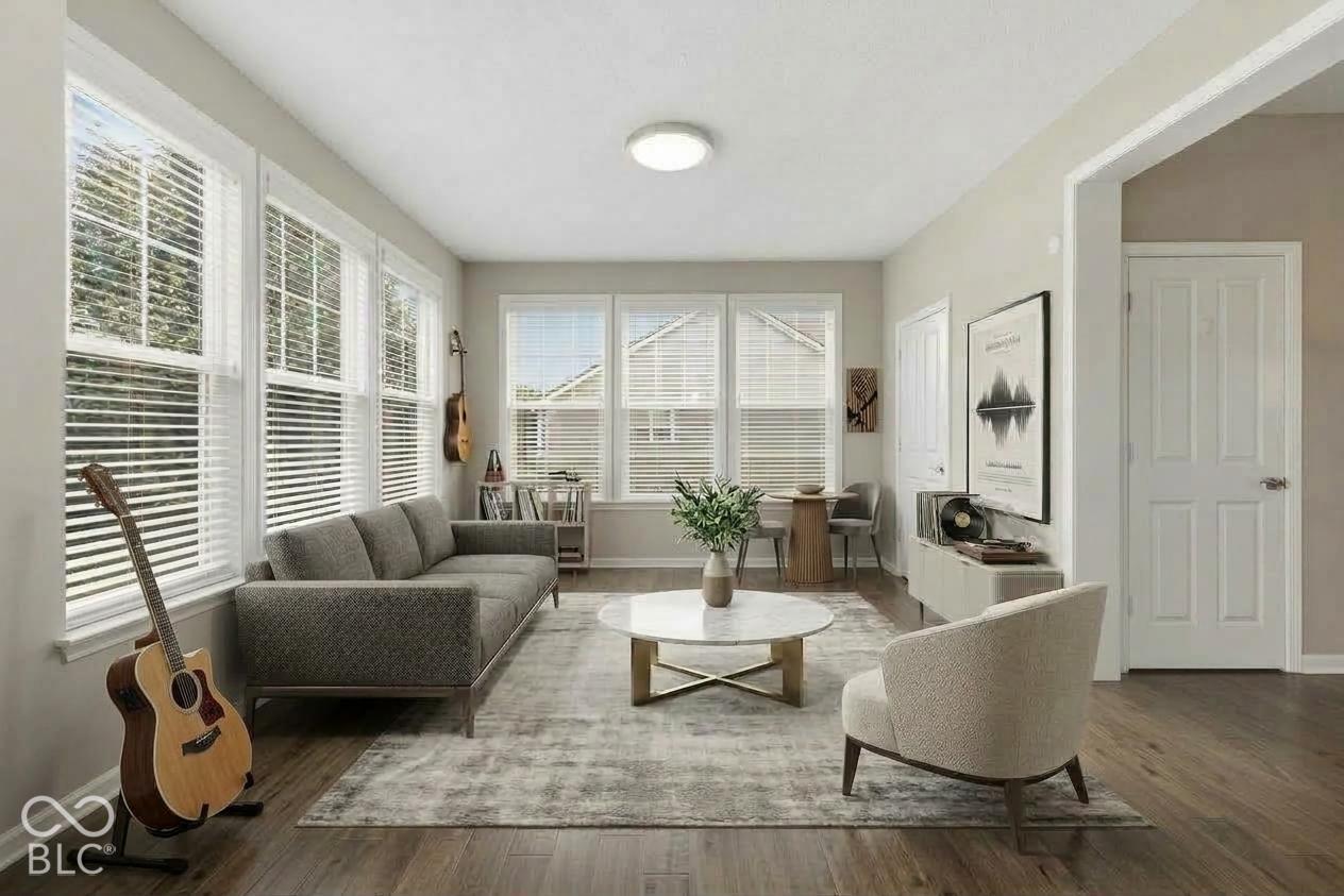 Staged living room with a gray sectional, round coffee table, and bright windows with white blinds.
