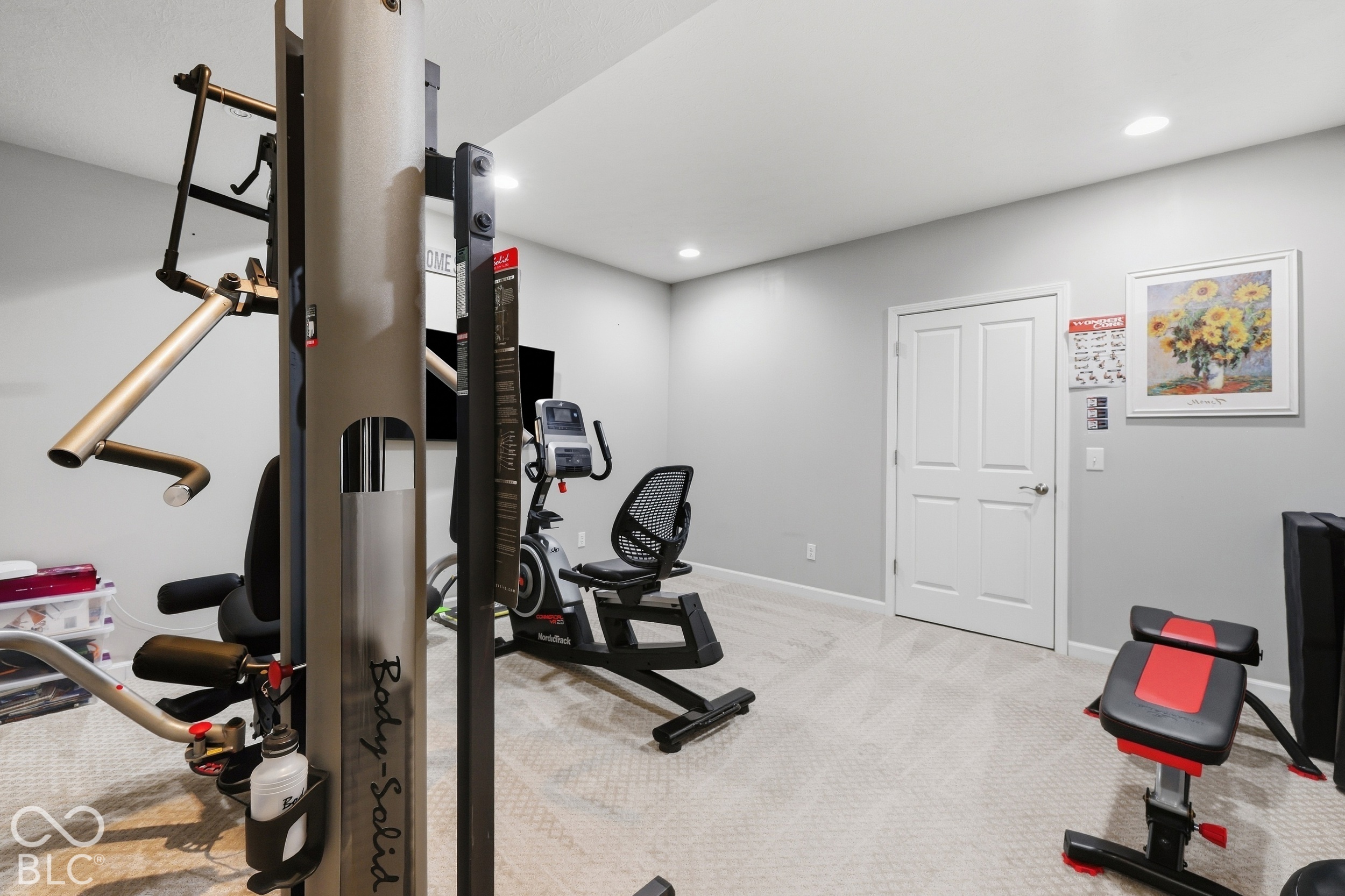 Home gym with a Body-Solid weight machine, NordicTrack bike, and red-and-black exercise bench.