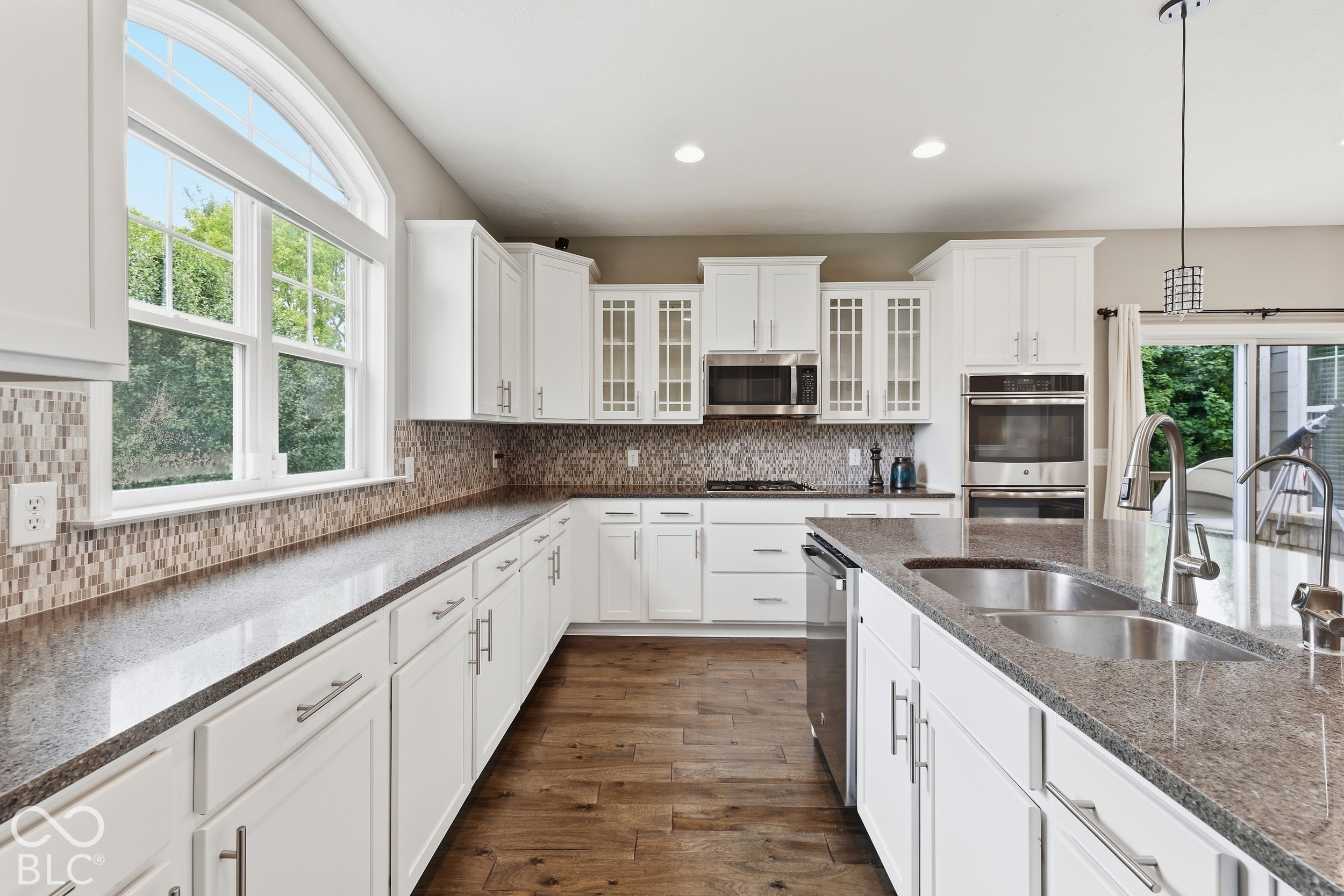 Bright kitchen with white cabinets, granite counters, stainless steel appliances, and a large island sink.