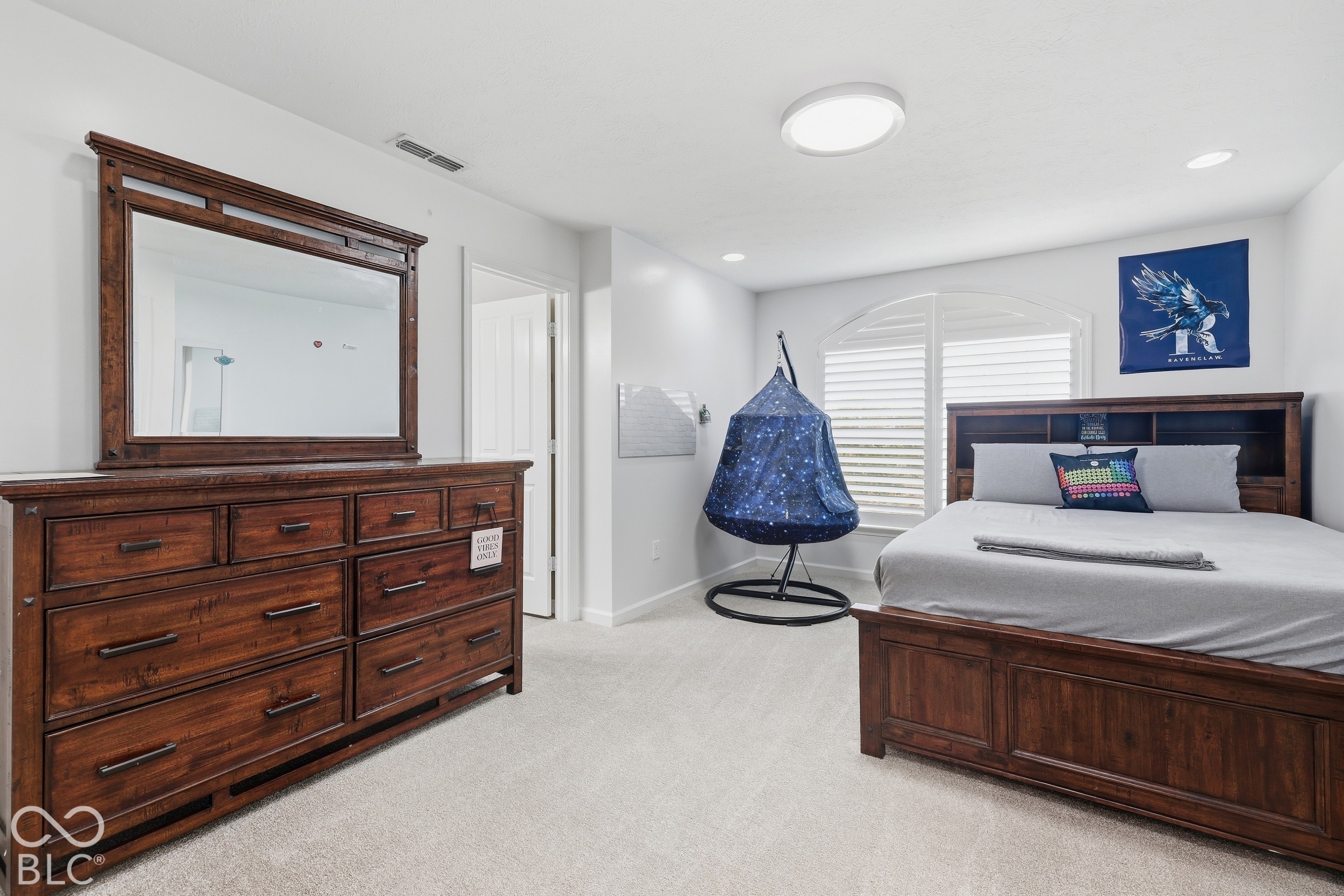 Furnished bedroom with dark wood furniture, a gray bed, arched shuttered window, and blue hanging chair.
