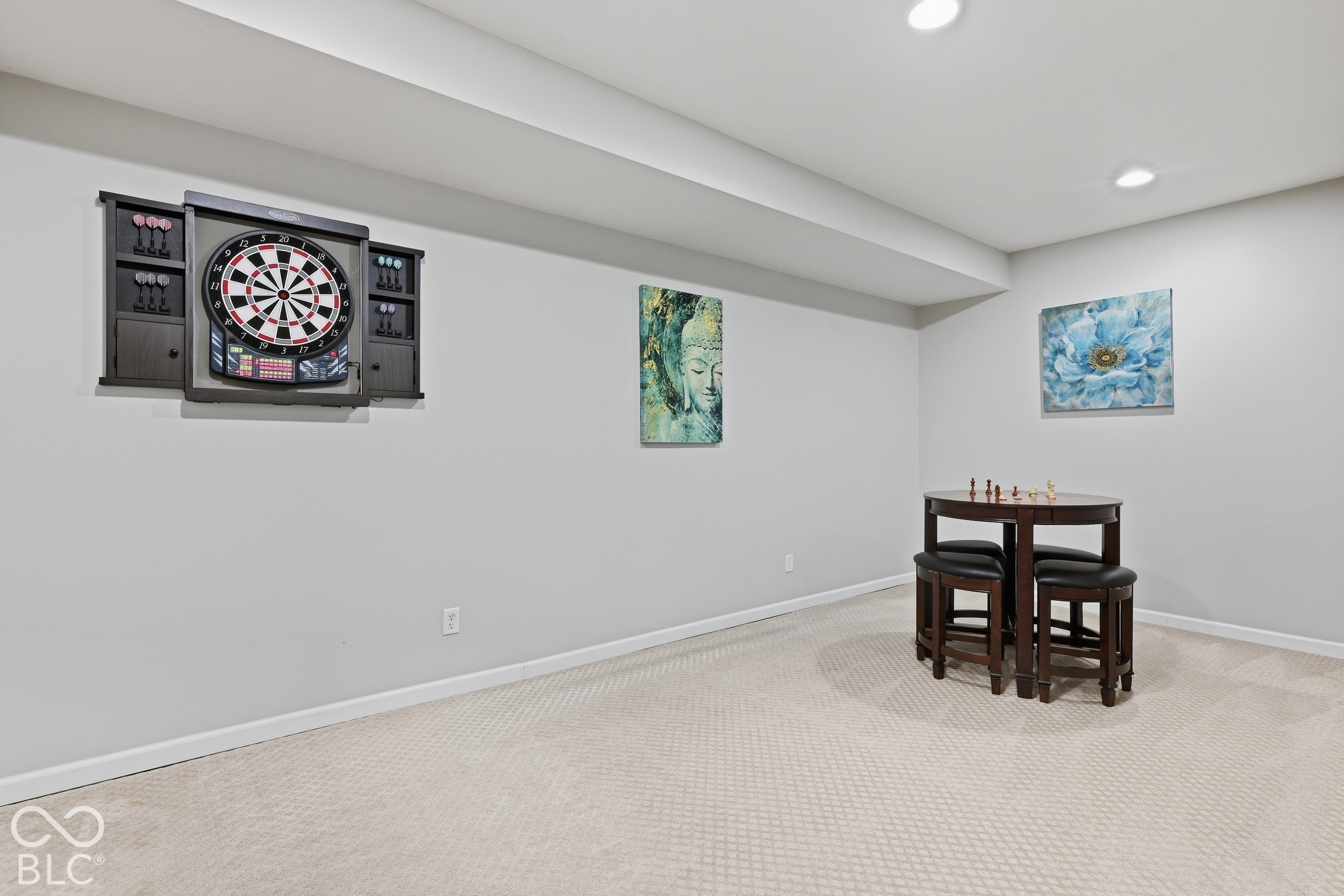 Basement game room with a wall-mounted dartboard and a chess table with stools.