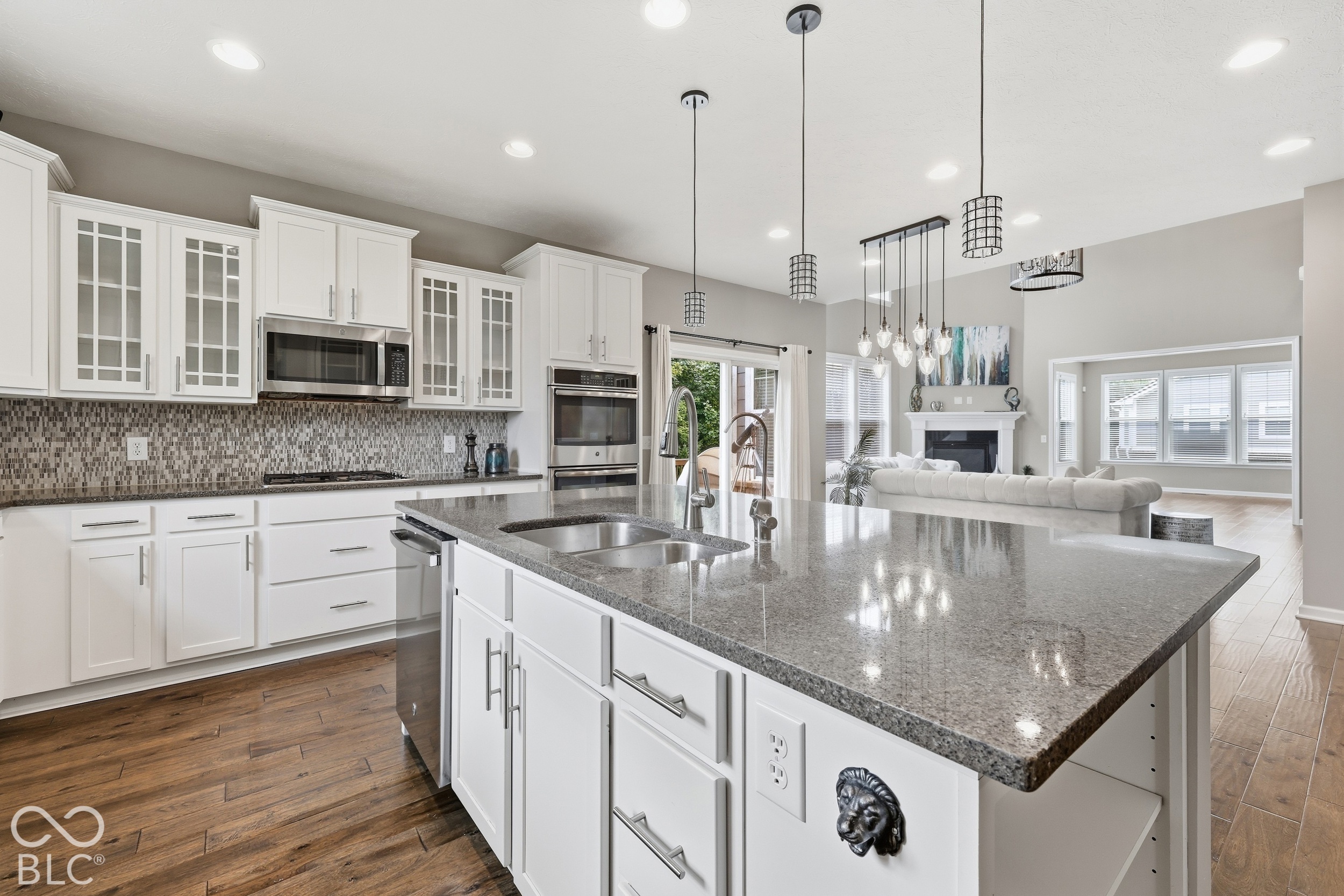 Open kitchen with a large granite island, white cabinets, and a view into the living room.