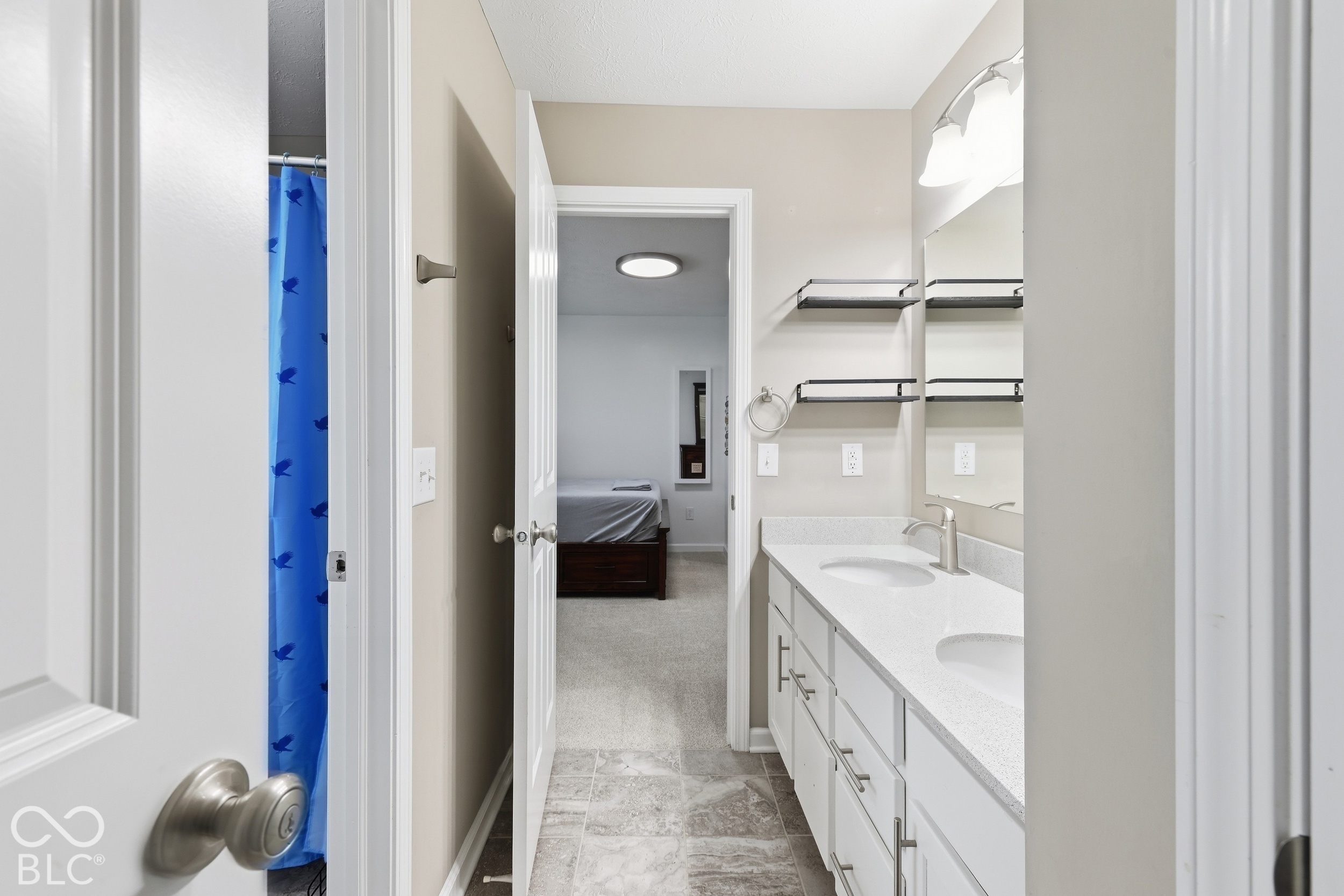 Bathroom with a white double-sink vanity, mirrored cabinets, and a blue shower curtain.
