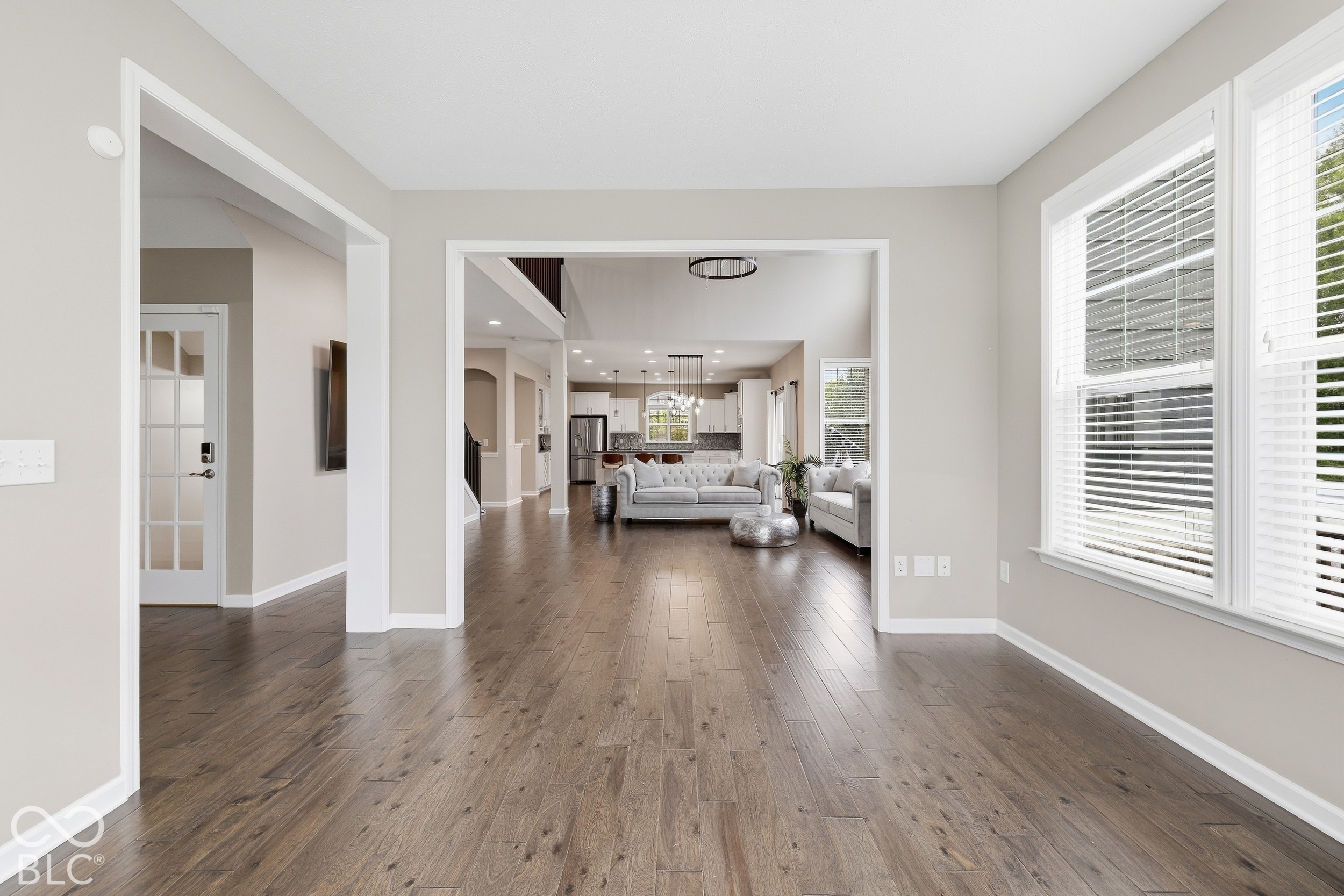 Furnished living room looking toward an open kitchen, with wide-plank hardwood floors and large windows.