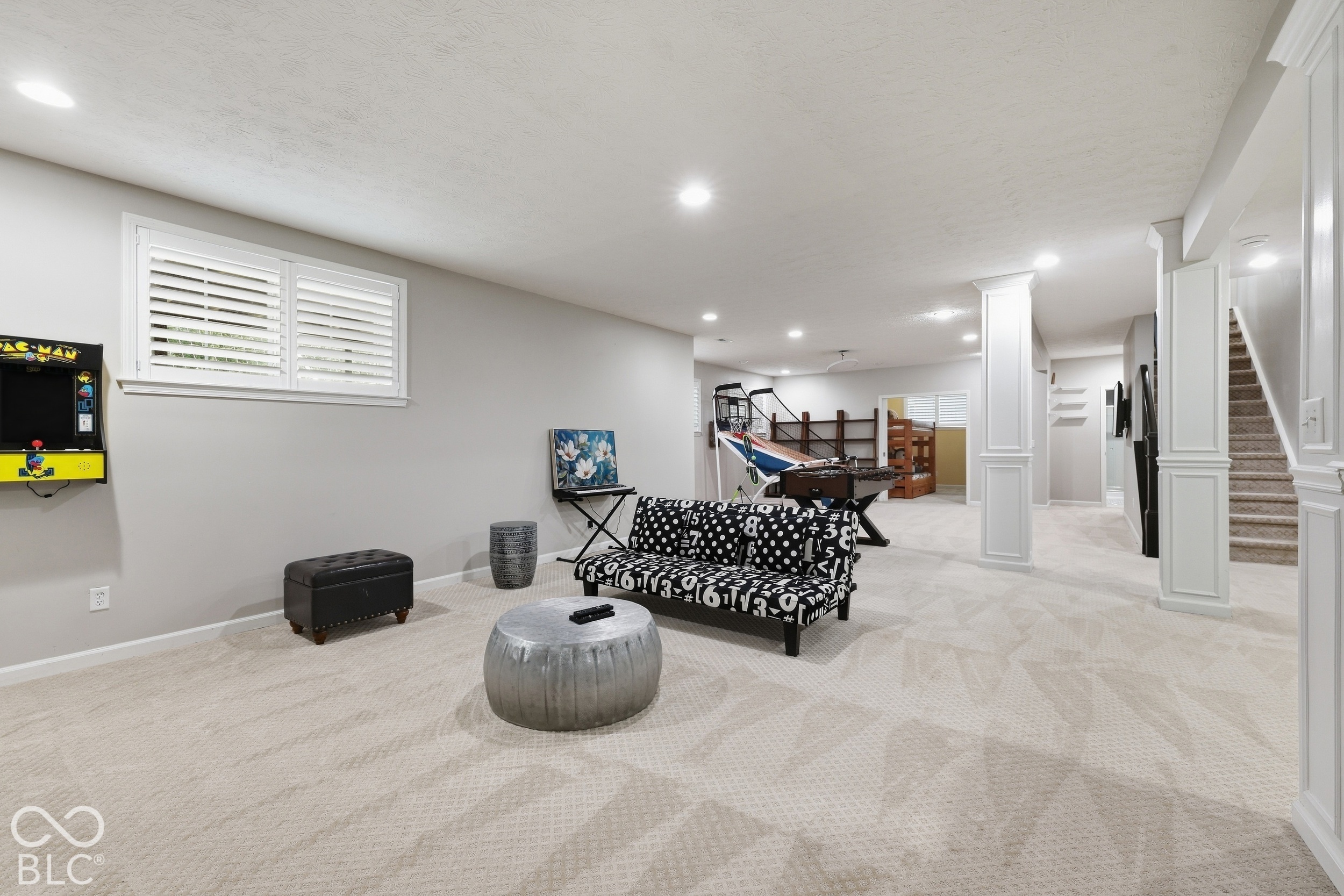 Basement recreation room with a Pac-Man arcade game, patterned sofa, and game tables.