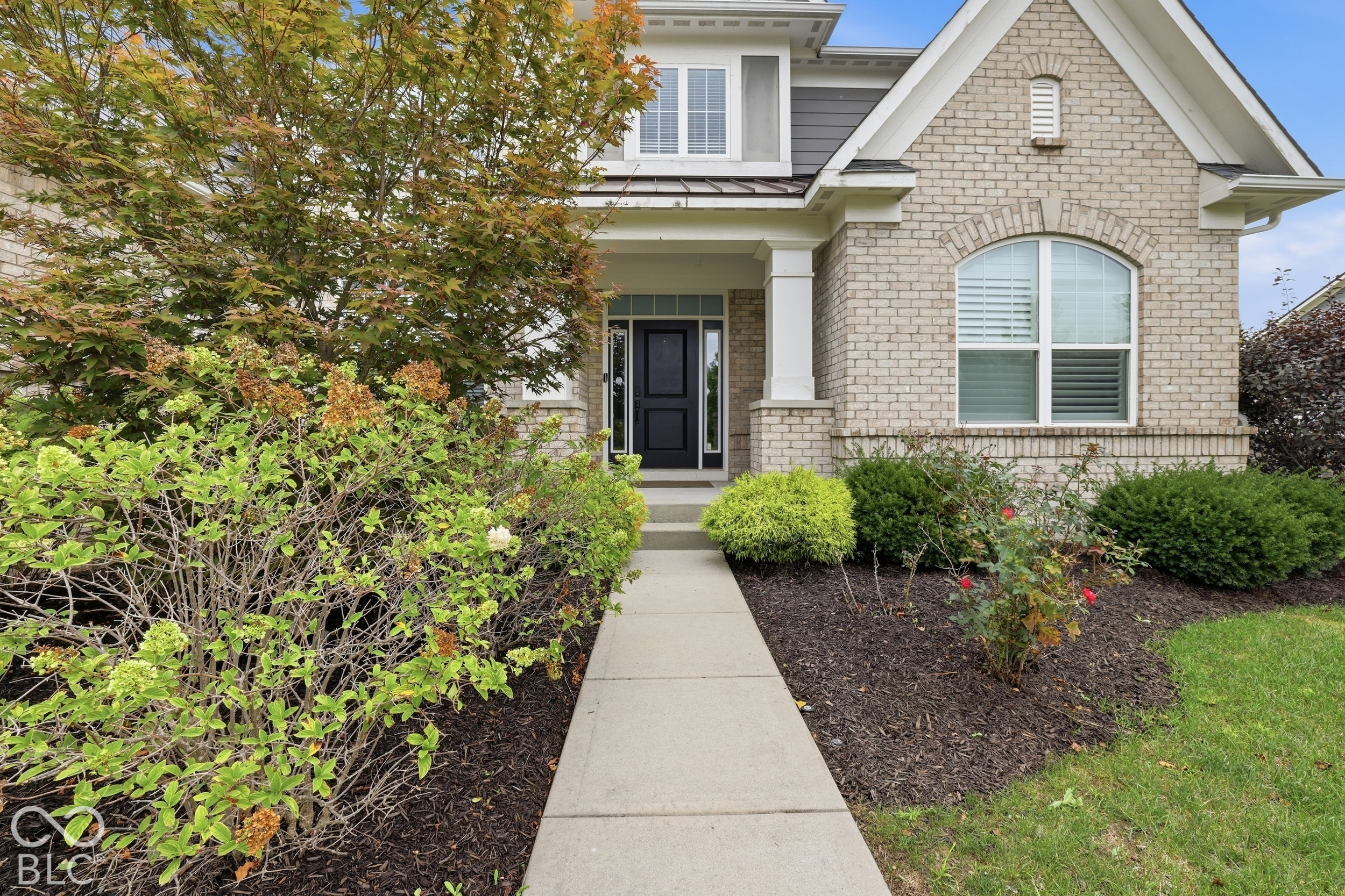 House entrance with a black front door, arched window, landscaped beds, and a walkway.