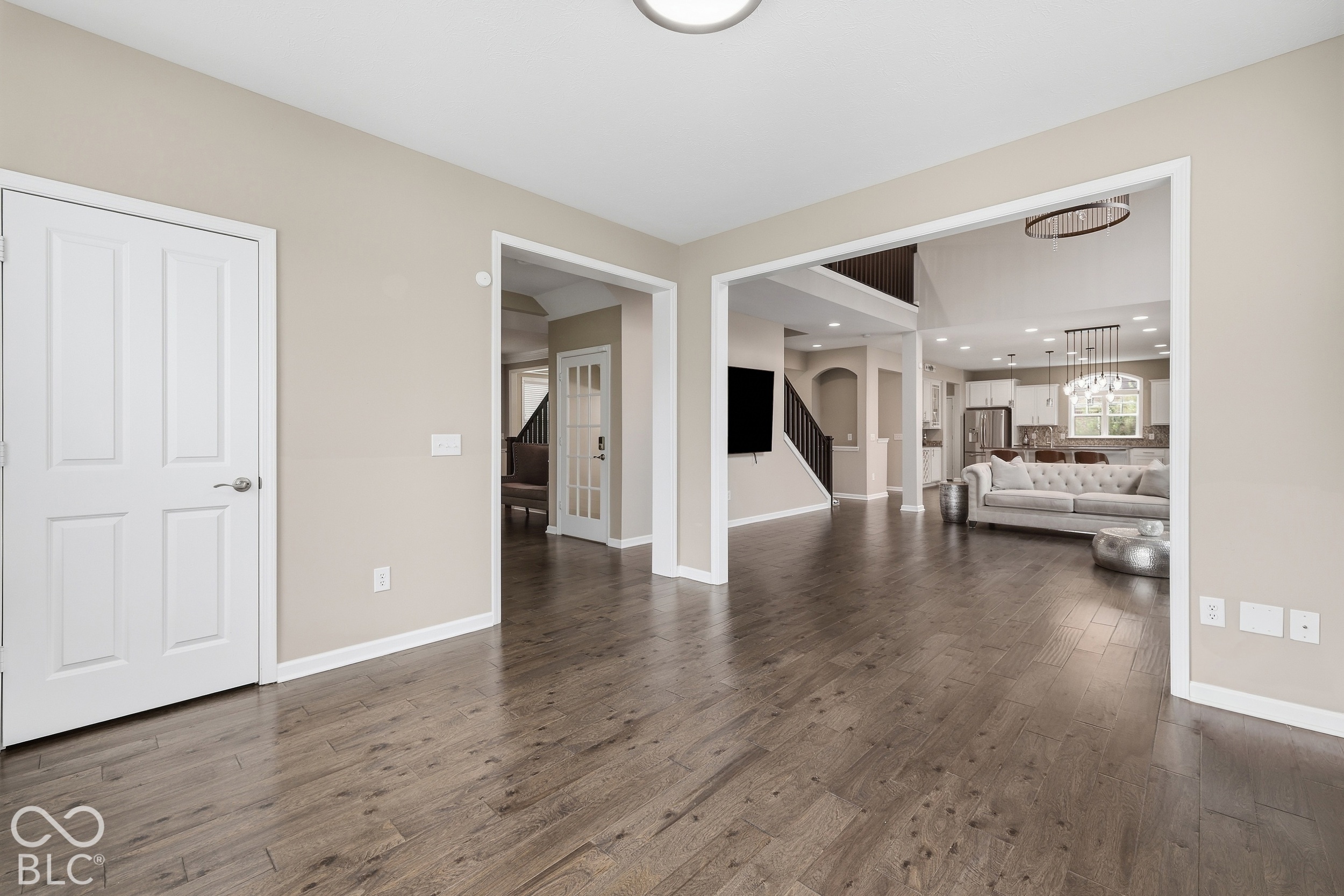 Open entry area with dark wood floors leading to a furnished living room and kitchen.