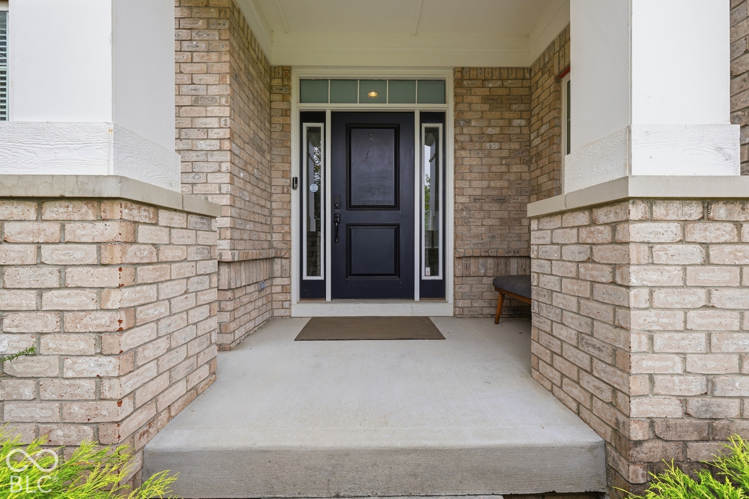 Covered brick front porch with a dark entry door, sidelights, and a bench.
