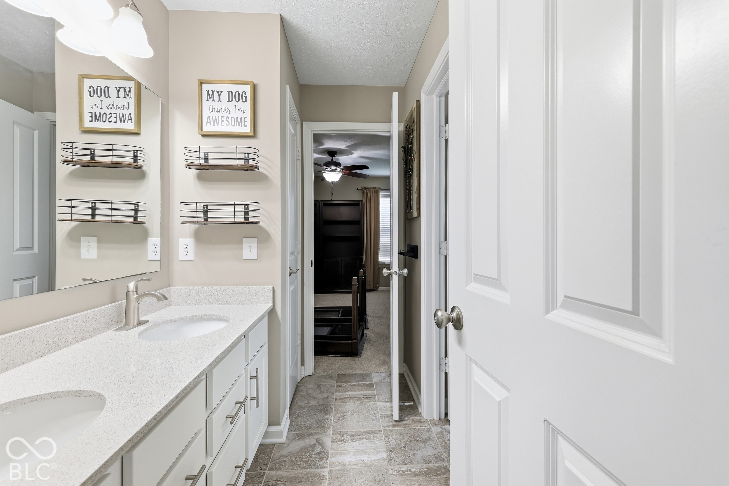 Bathroom vanity with two sinks, white cabinetry, metal wall shelves, and gray tile flooring.