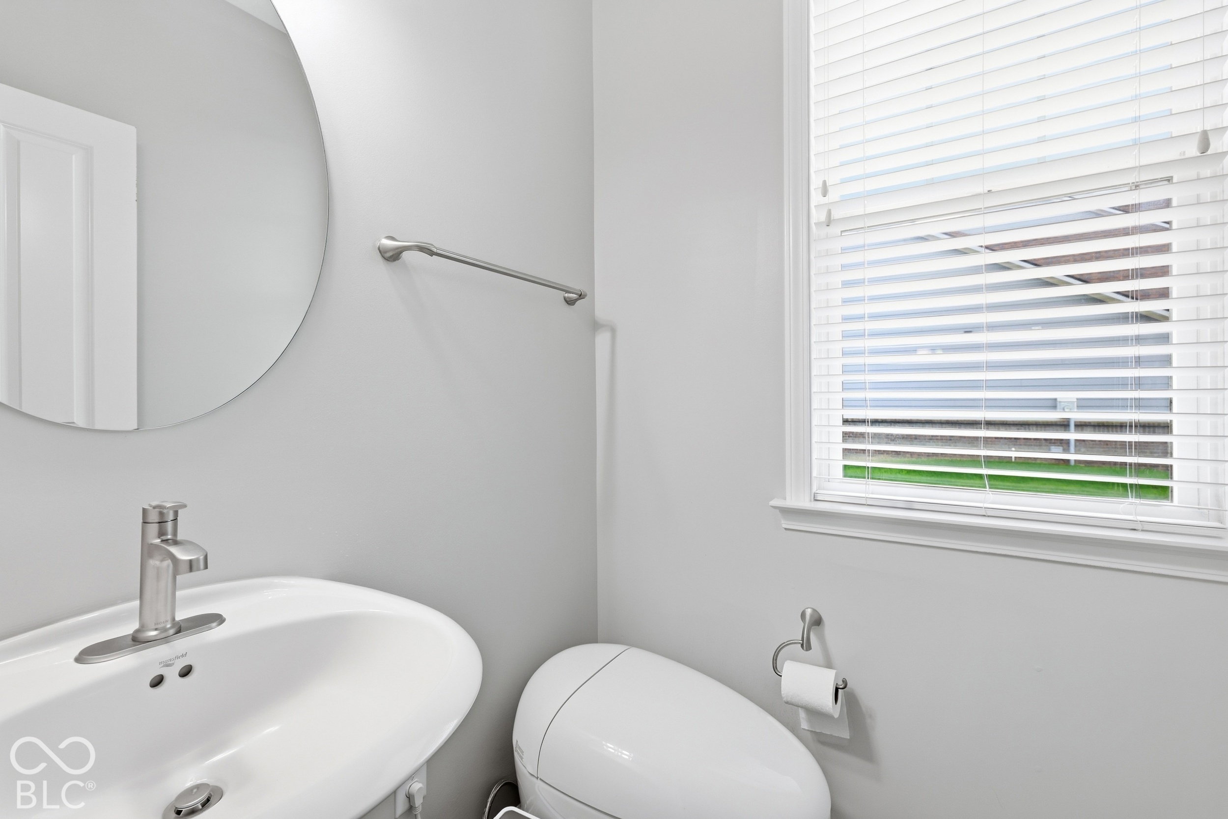 Bathroom with a white sink and toilet beneath a window with blinds.