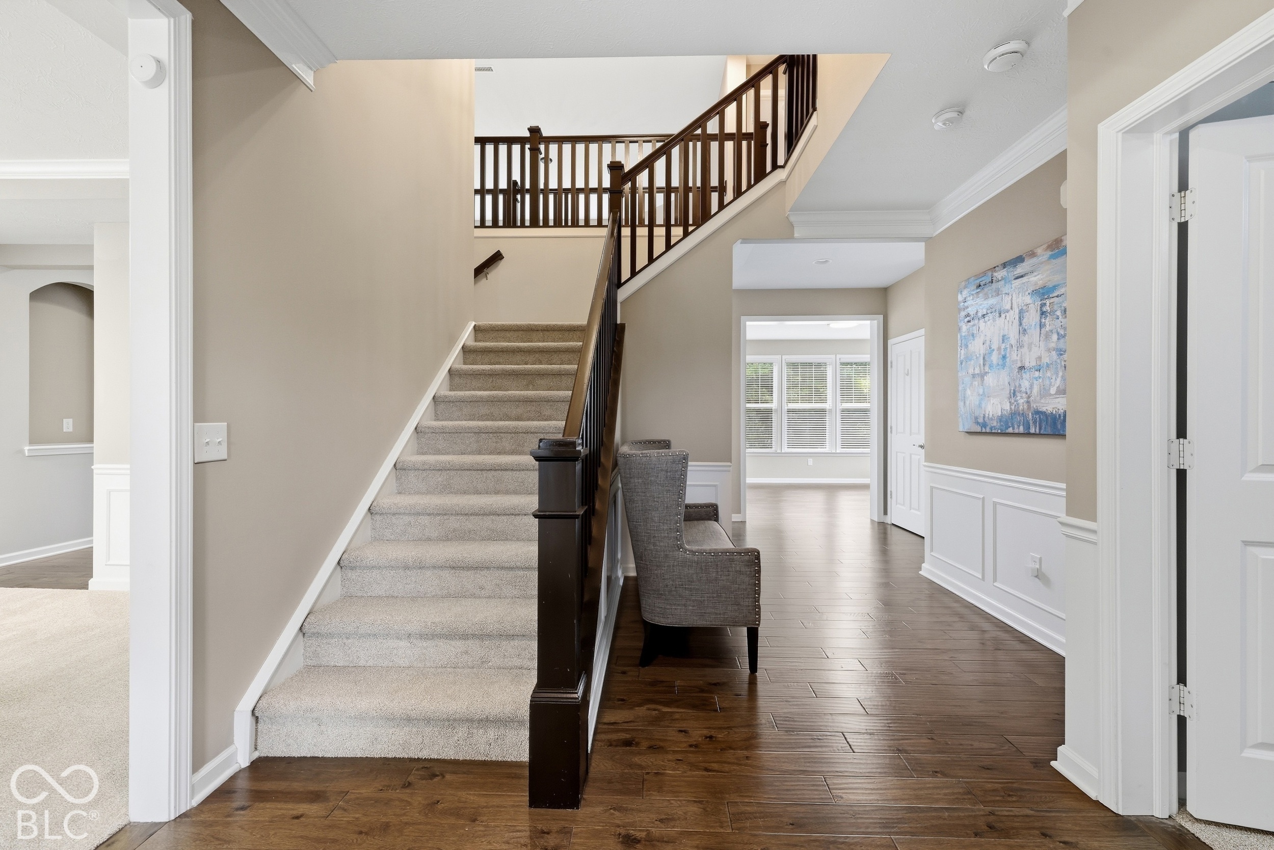 Entry foyer with carpeted staircase, dark wood railings, hardwood floors, and a chair.