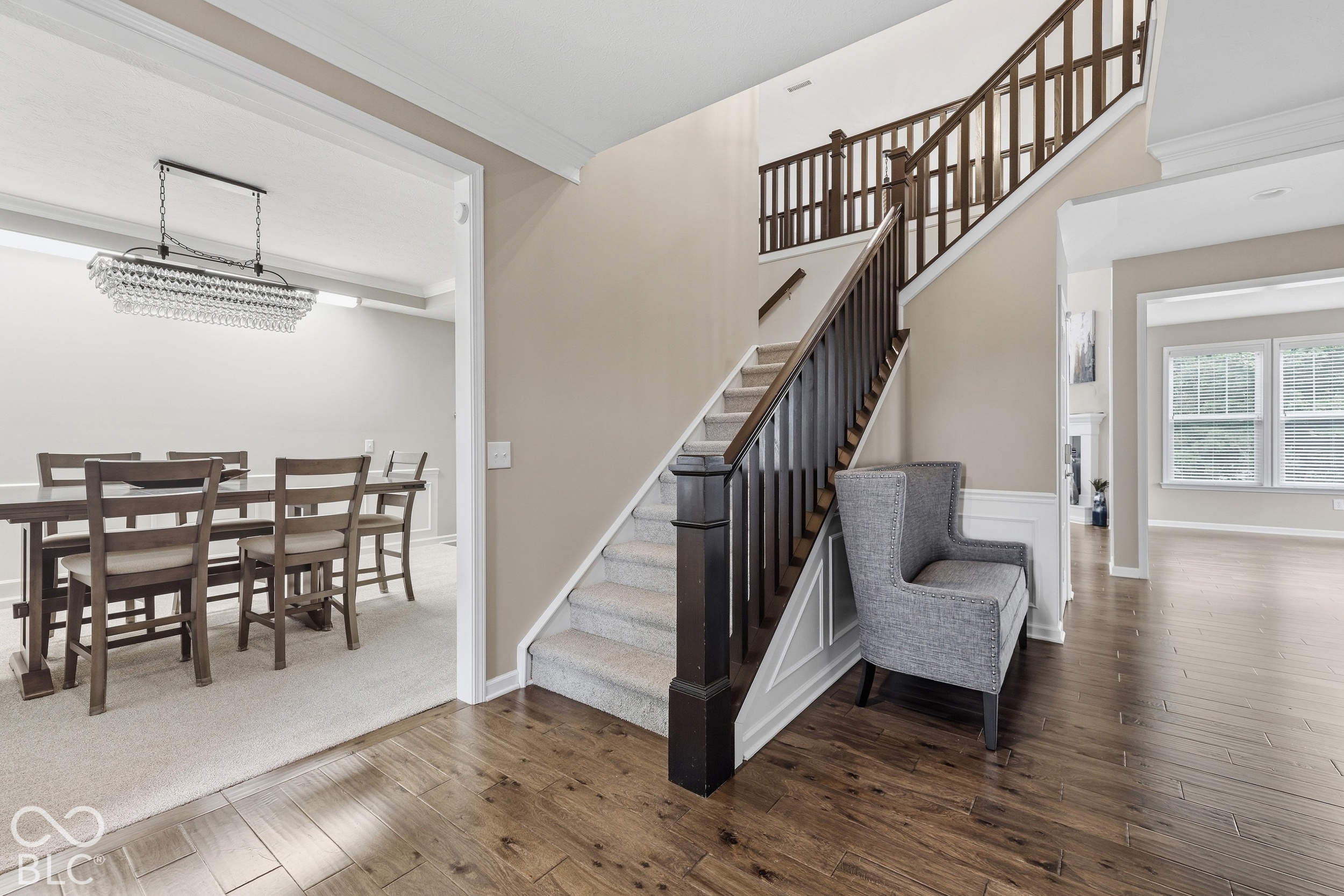 Foyer staircase with dark railings, gray chair, and adjoining dining room with chandelier.