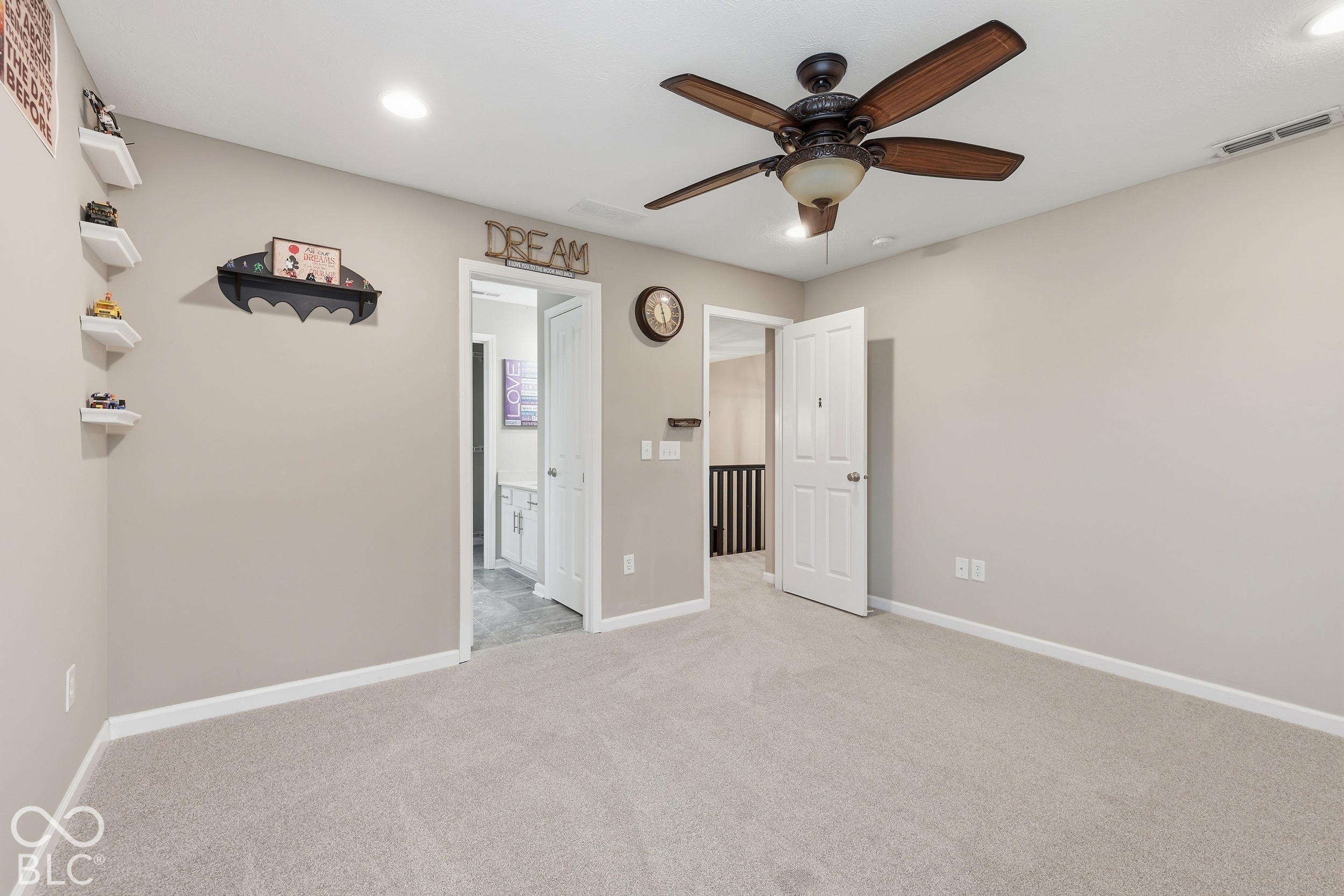 Carpeted bedroom with a dark wood ceiling fan and open doors to a bathroom and hallway.