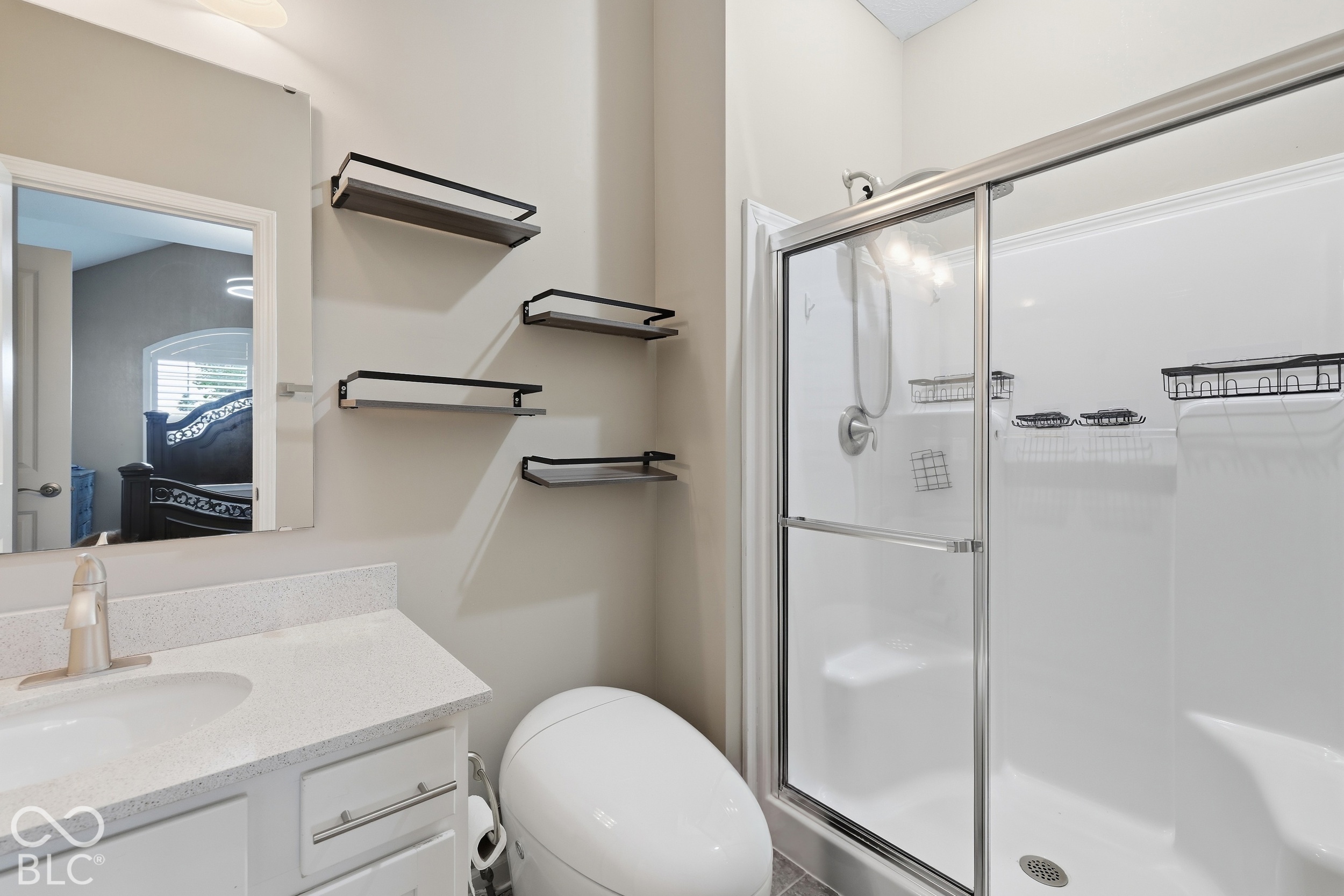 Bathroom with a glass-enclosed tub and shower, white vanity, and four black floating shelves.