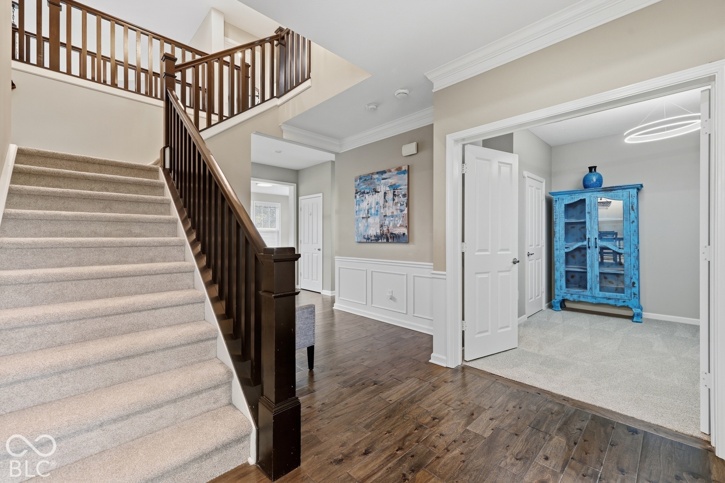 Foyer with carpeted staircase, dark wood railing, hardwood floors, and a bright blue cabinet in the adjoining room.