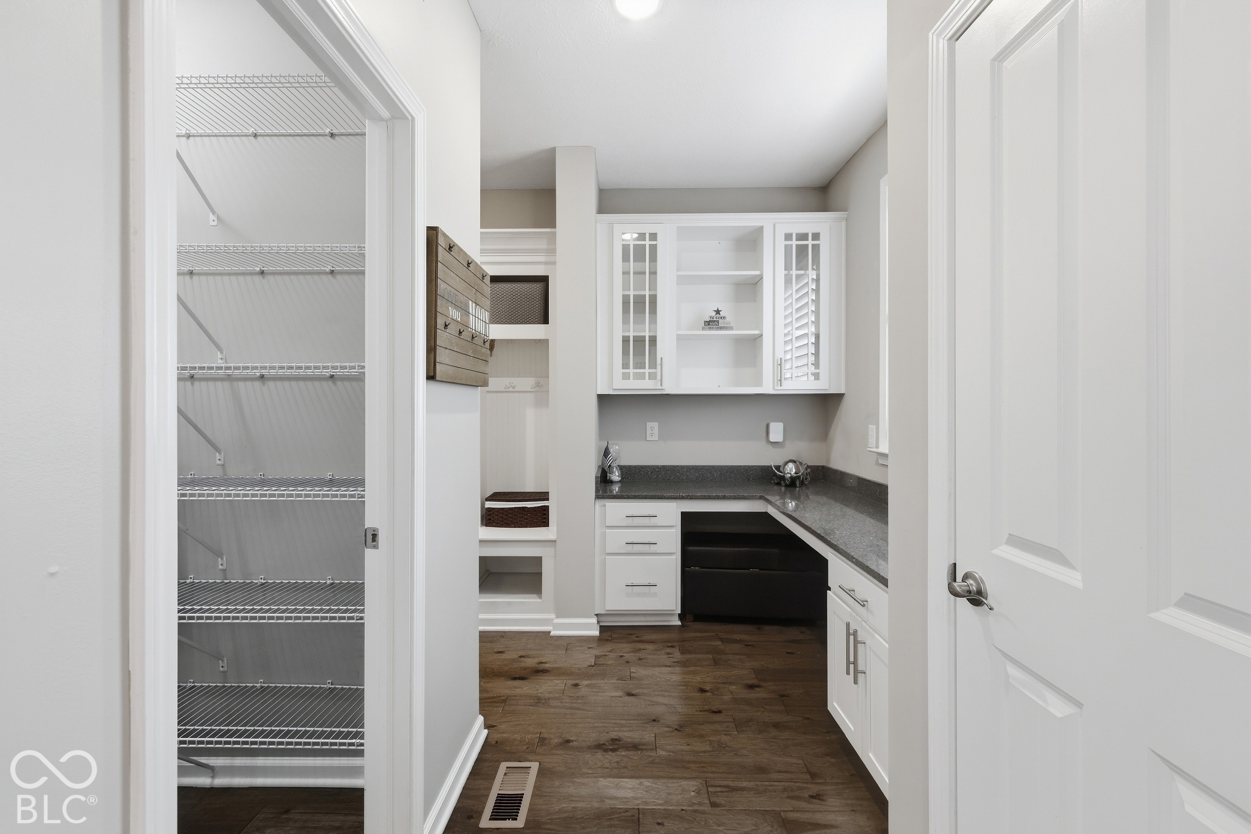 Home office with white built-in cabinets and dark counters beside a walk-in closet with wire shelving.