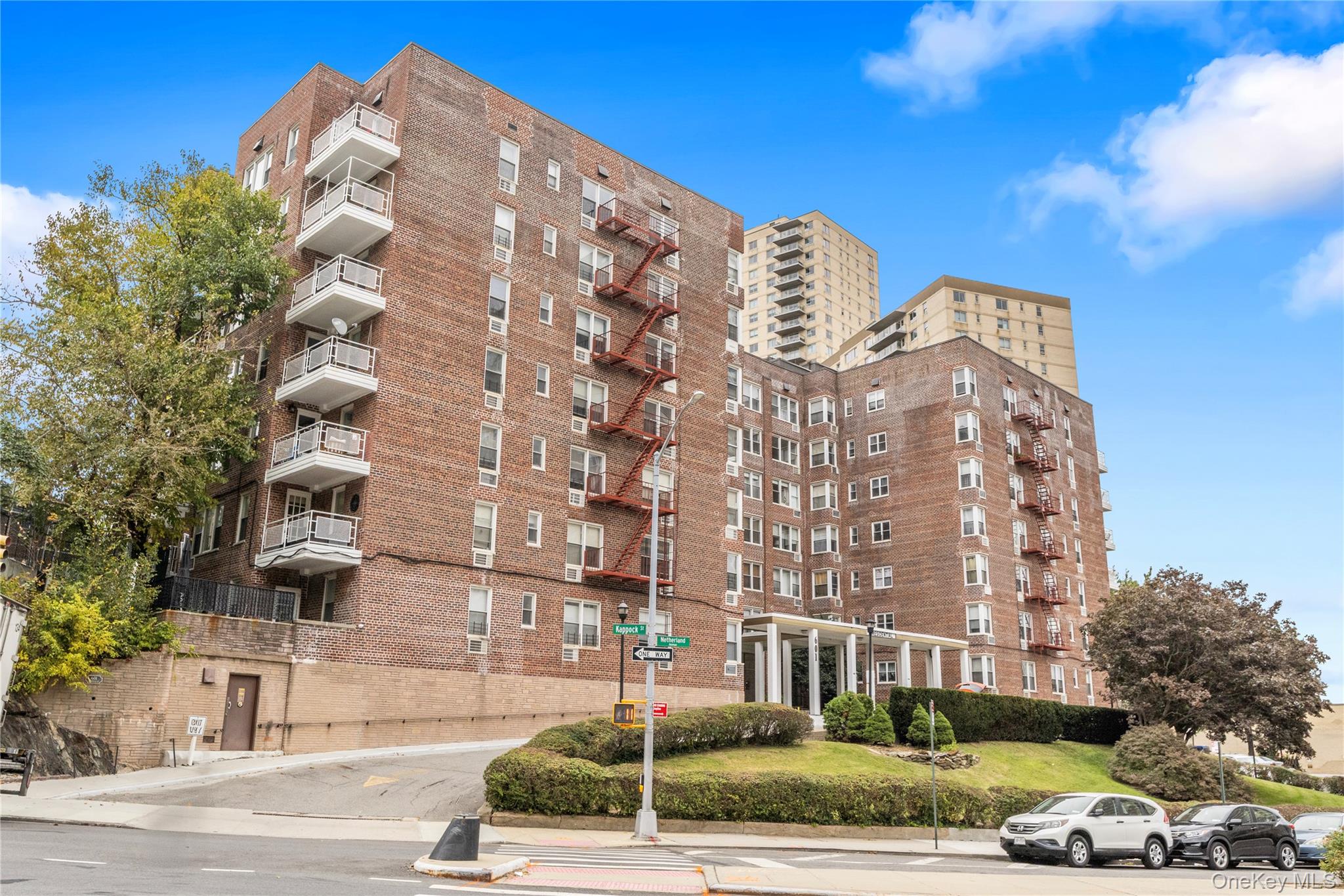 Red-brick apartment building with white balconies, red fire escapes, and a landscaped corner entrance.