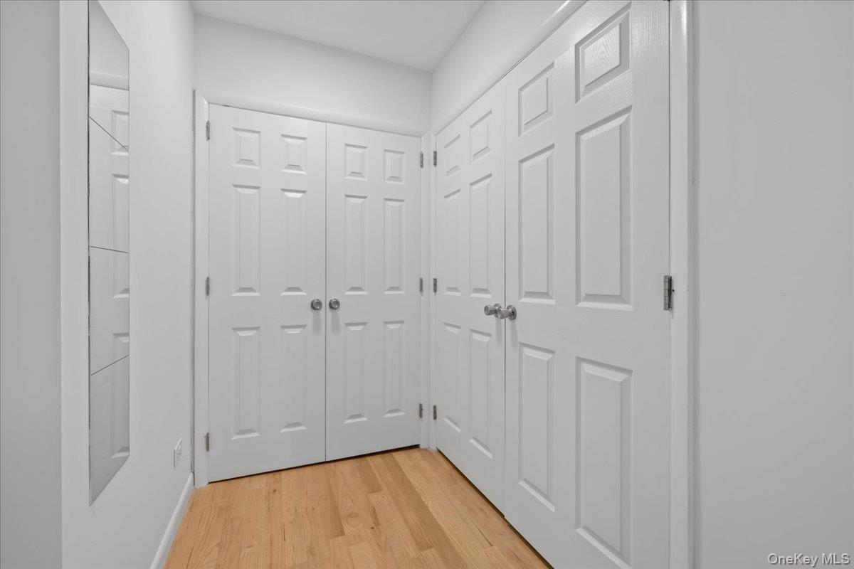 Hallway with multiple white paneled closet doors, a wall mirror, and hardwood flooring.