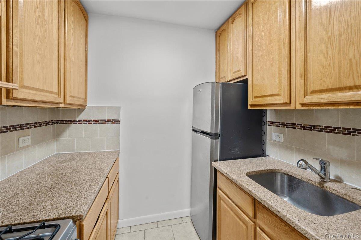 Narrow kitchen with light wood cabinets, speckled counters, stainless refrigerator, and sink.