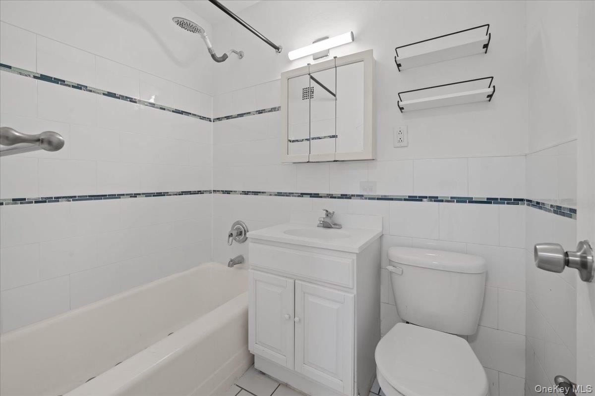 White-tiled bathroom with a bathtub, vanity, toilet, and blue mosaic accent bands.