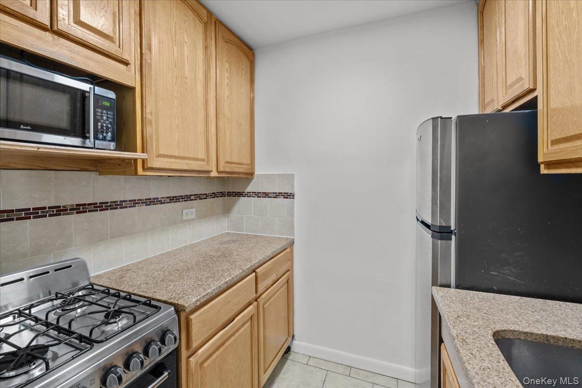 Galley kitchen with wood cabinets, a stainless gas range, and a refrigerator.