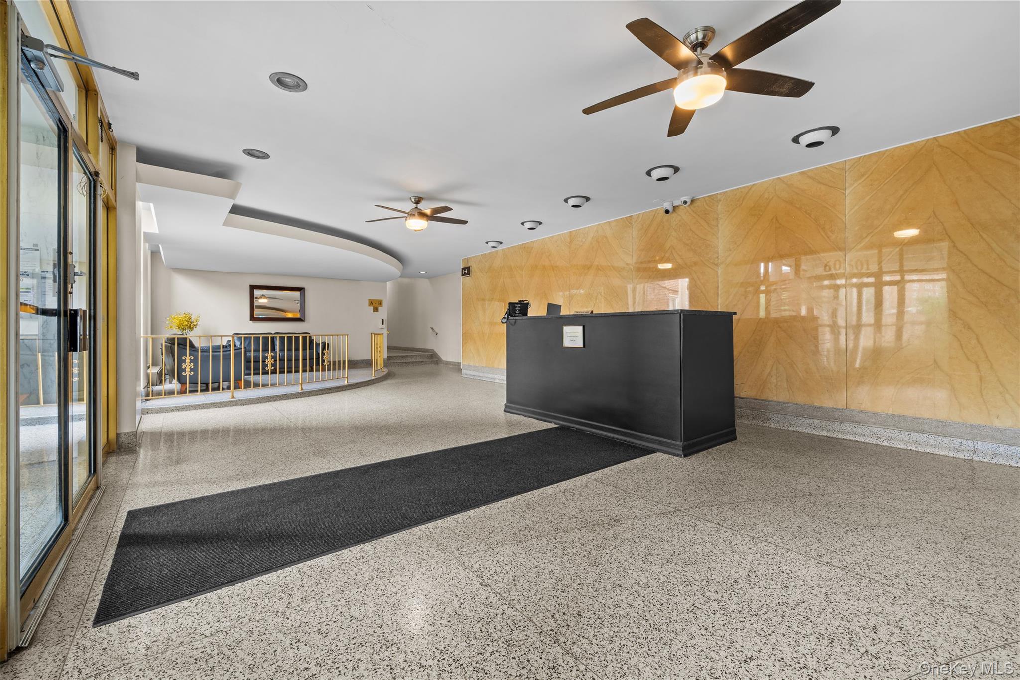 Residential lobby with a black reception desk, gold-toned marble wall, and seating behind a railing.
