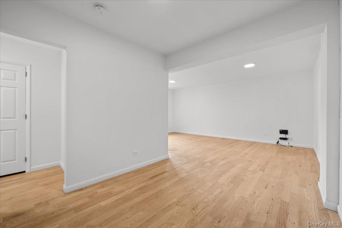 Vacant living area with light hardwood floors, white walls, and recessed ceiling lights.